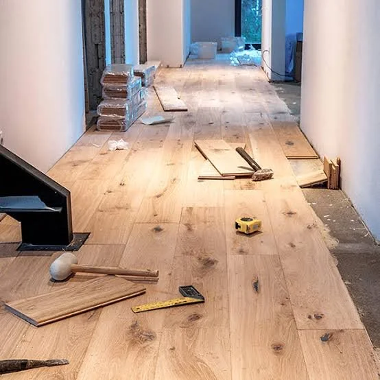 Interior of a house under construction with hardwood flooring, construction tools, and materials scattered on the floor.