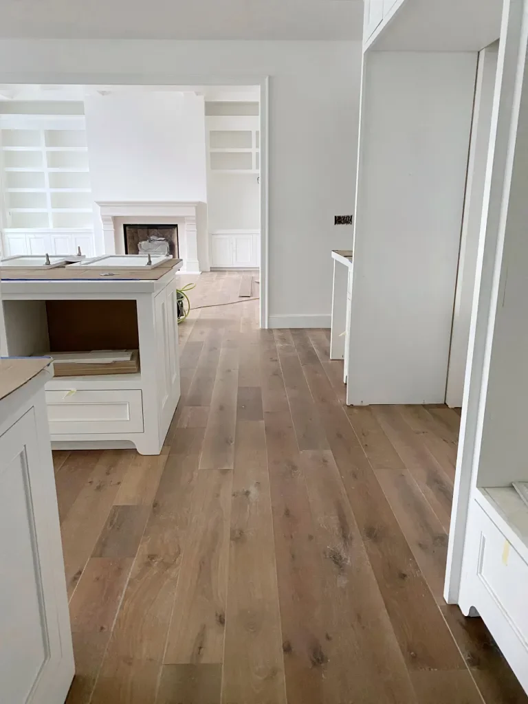 Empty room with wooden flooring, white built-in cabinets, and a fireplace in the background.