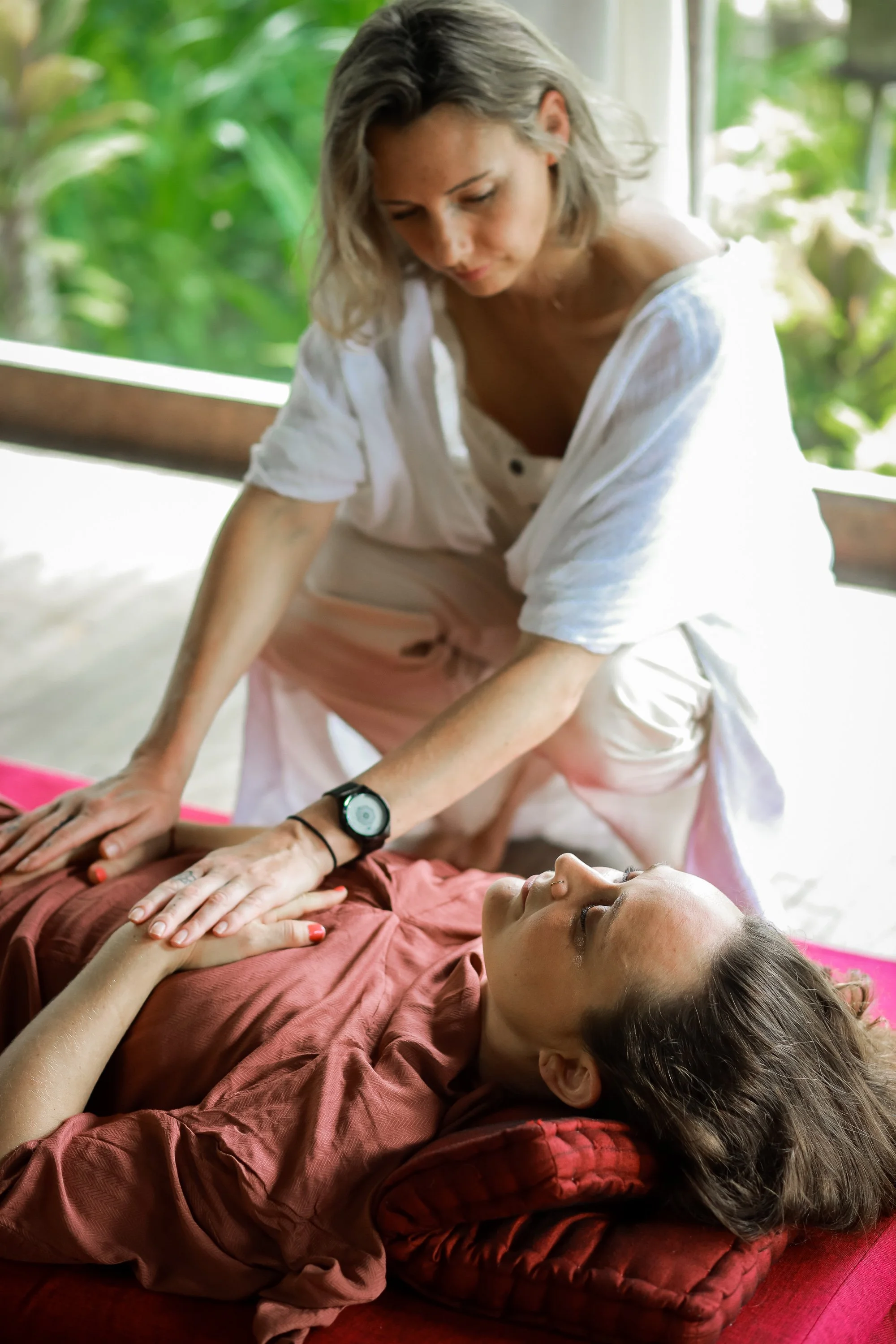 A woman receiving a massage from another woman in a peaceful, green, outdoor setting.
