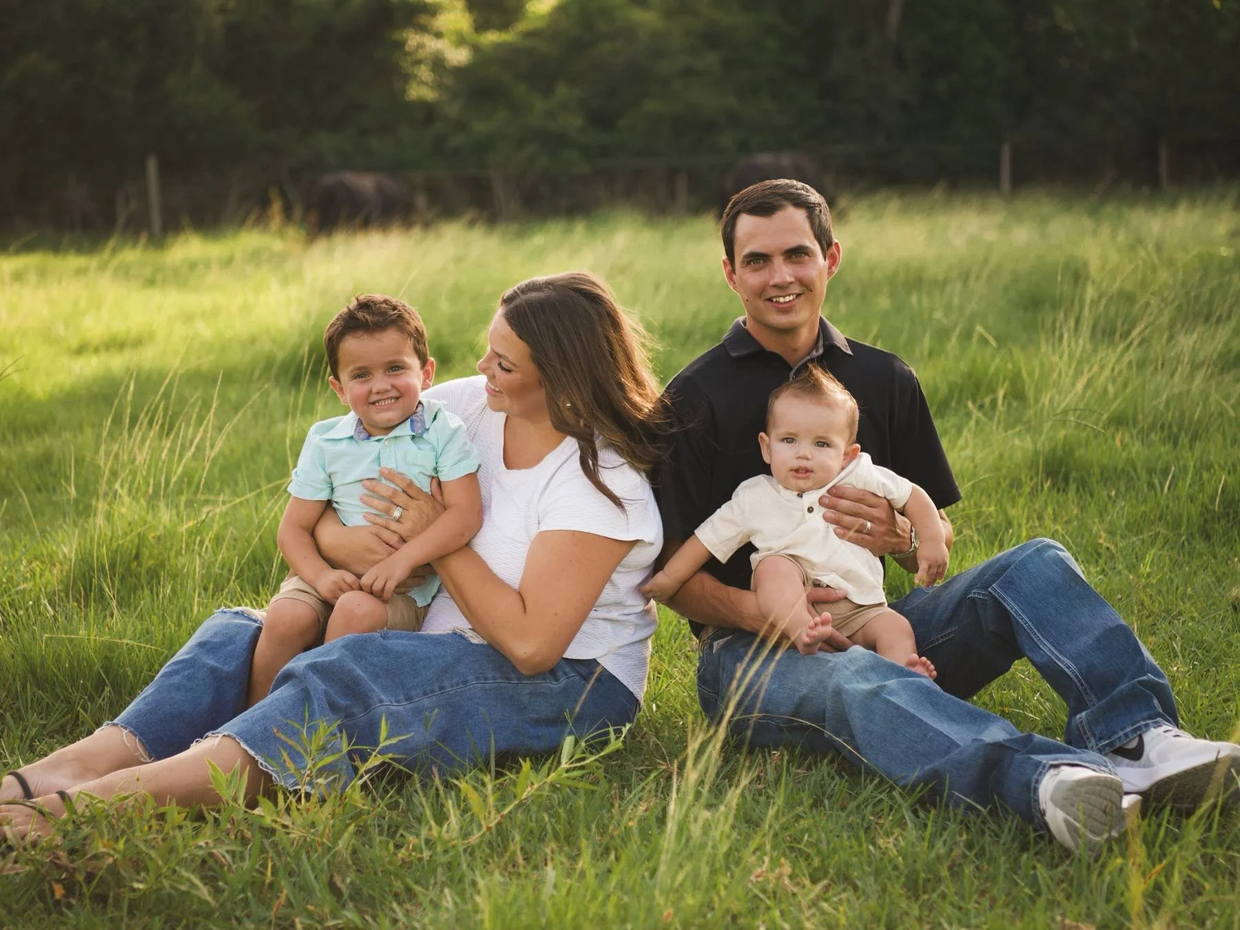 A family of four sitting on grass in a park, smiling and enjoying the outdoors during daylight.