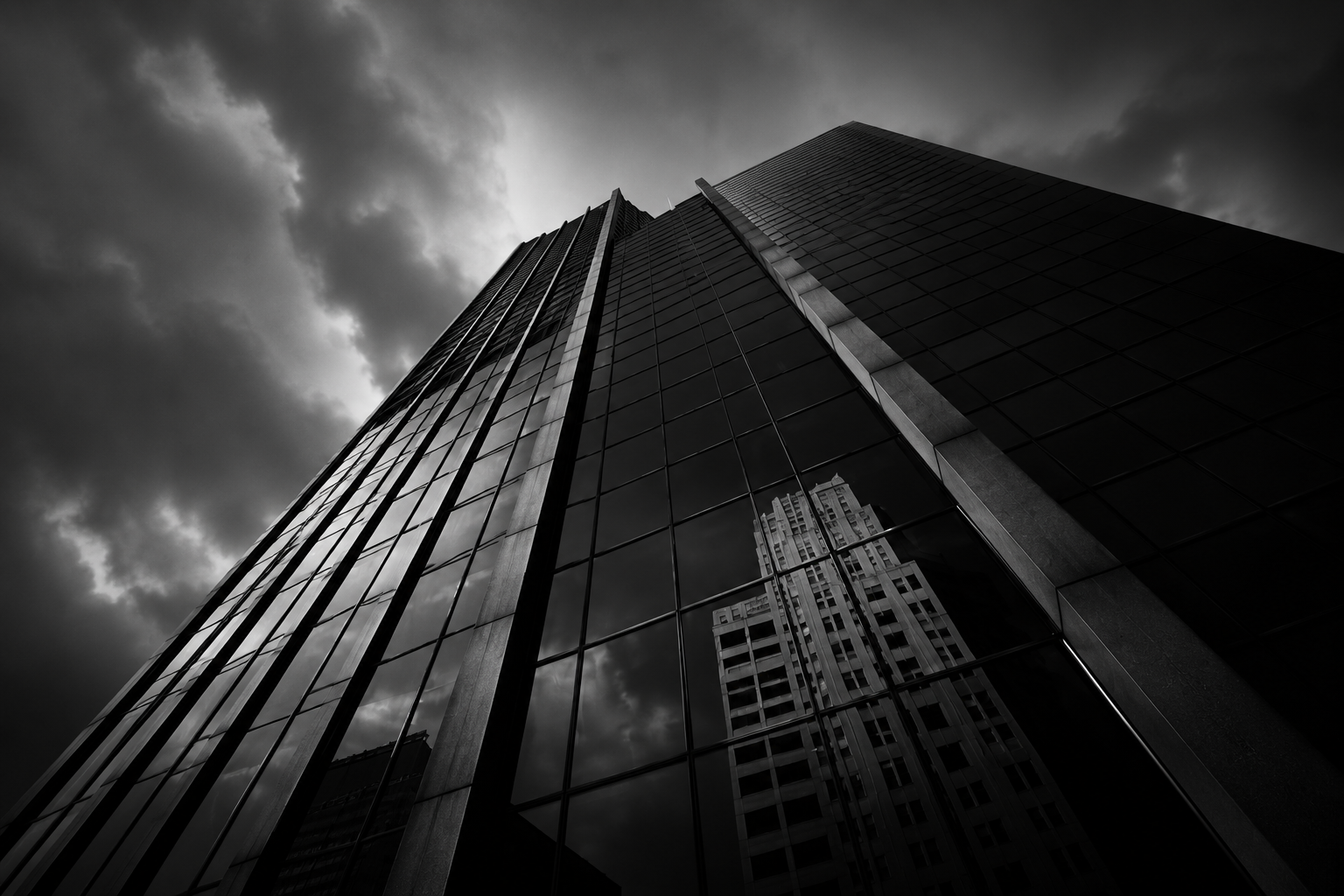A tall glass skyscraper reflecting other buildings and cloudy sky in downtown city.