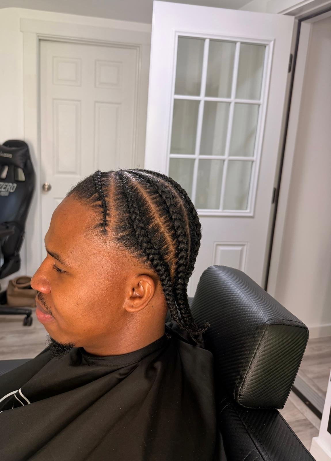 A man with braided hairstyle sitting in a barber's chair.