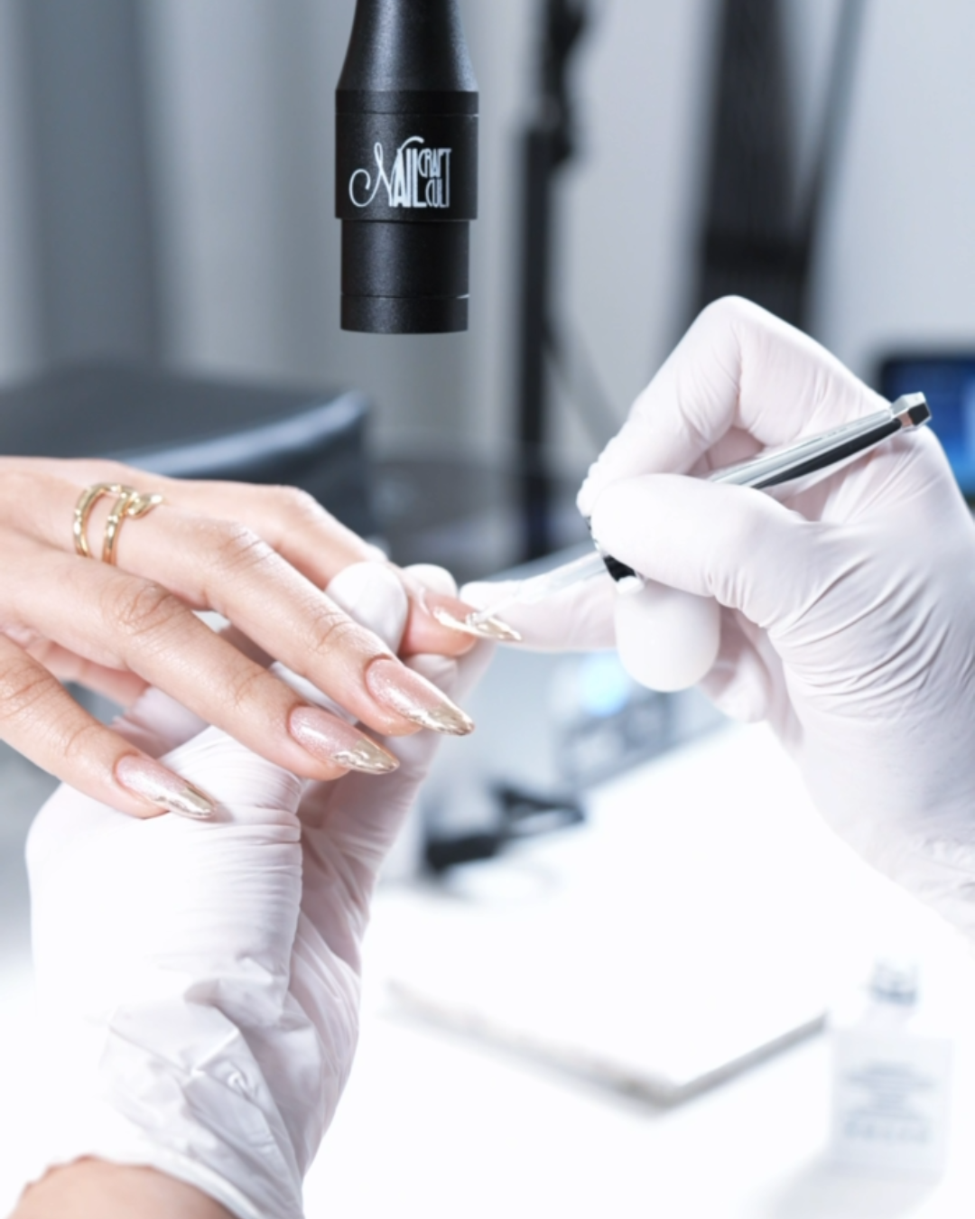 A person receiving a manicure, with a nail technician writing in a notebook, in a clinical setting with laboratory equipment in the background.