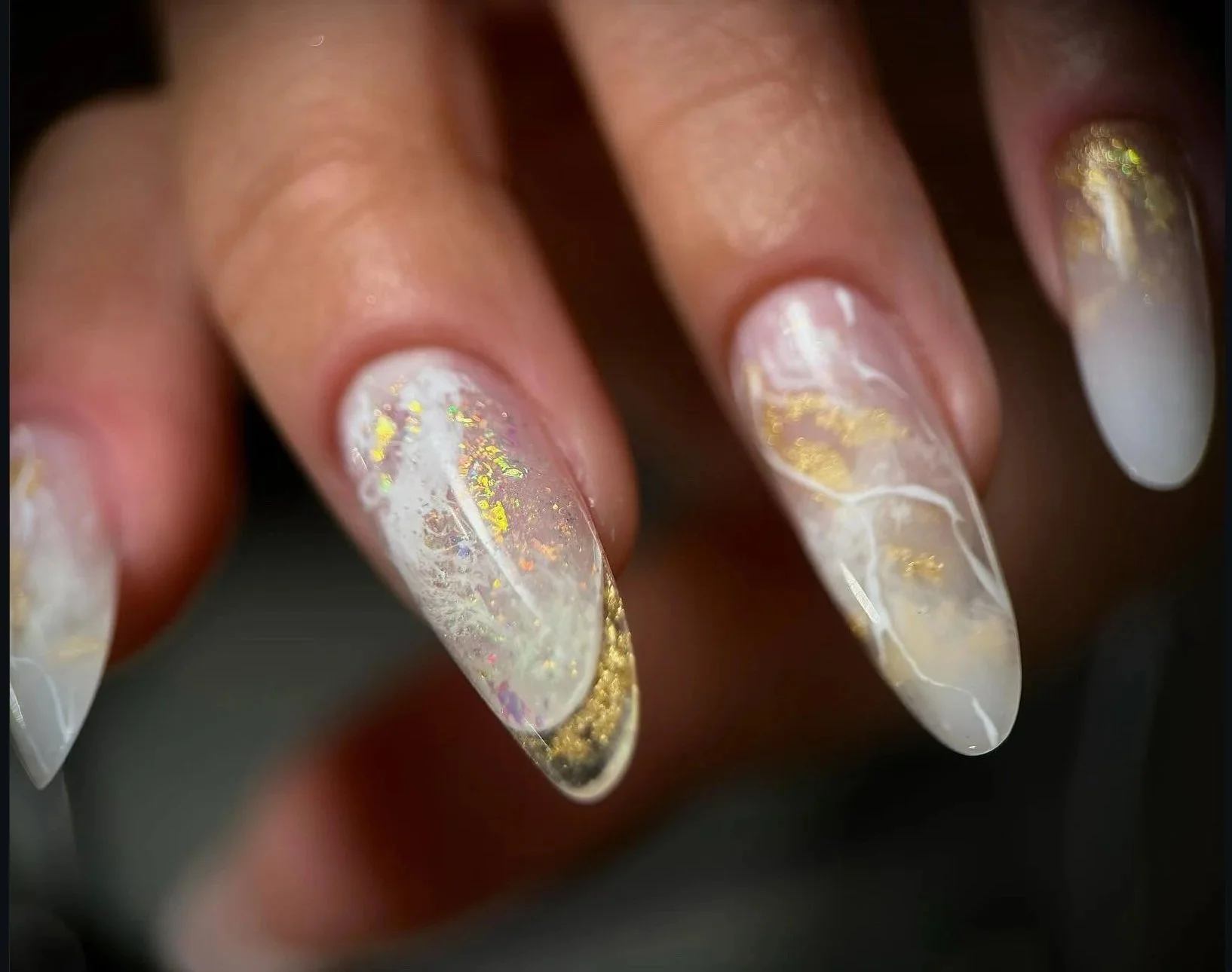 Close-up of decorated hard gel nails with a marble pattern, white and gold accents, and holographic details.