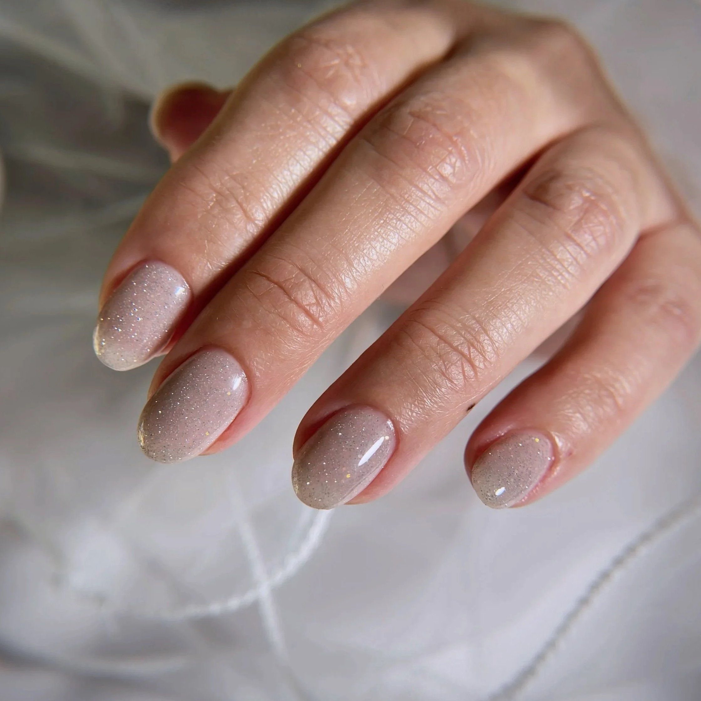 Close-up of a person's hand showing painted and glittery nails, with the skin and nails in focus.