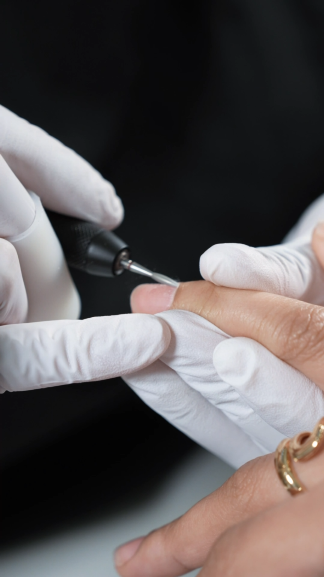A person receiving a Russian manicure with a diamond bit on their finger from a nail artist wearing white gloves.
