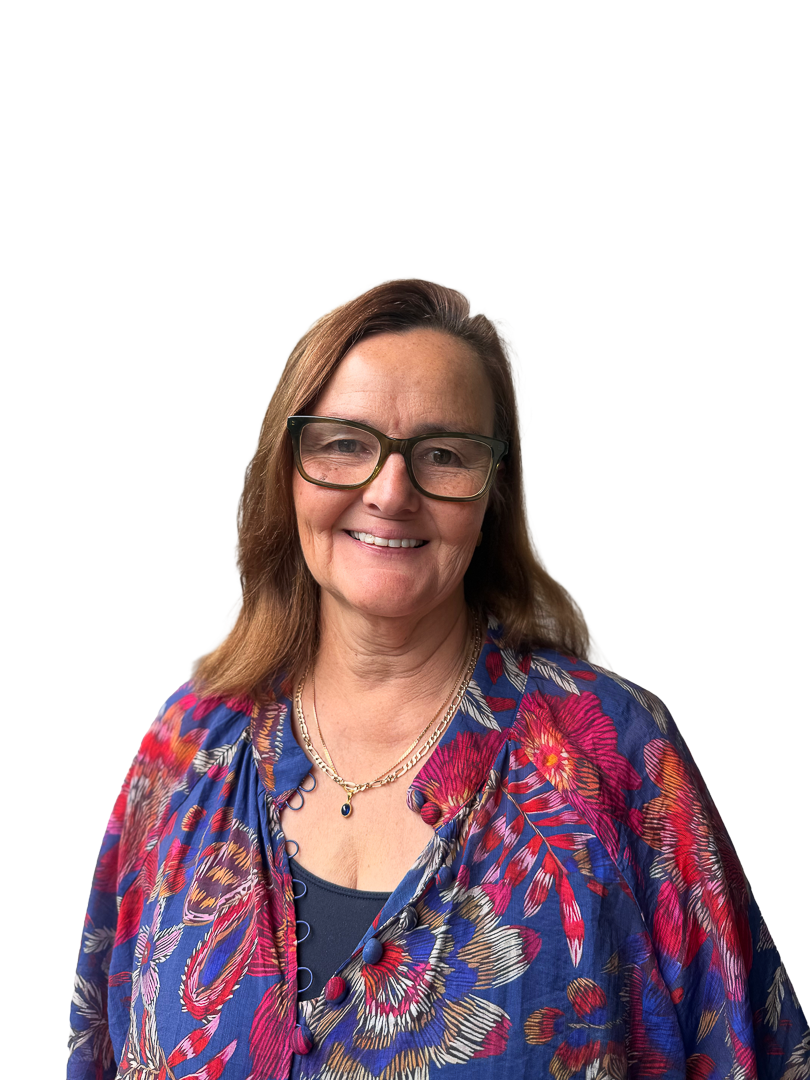 A woman with brown hair, wearing glasses, a blue patterned blouse, and a layered necklace, smiling at the camera.