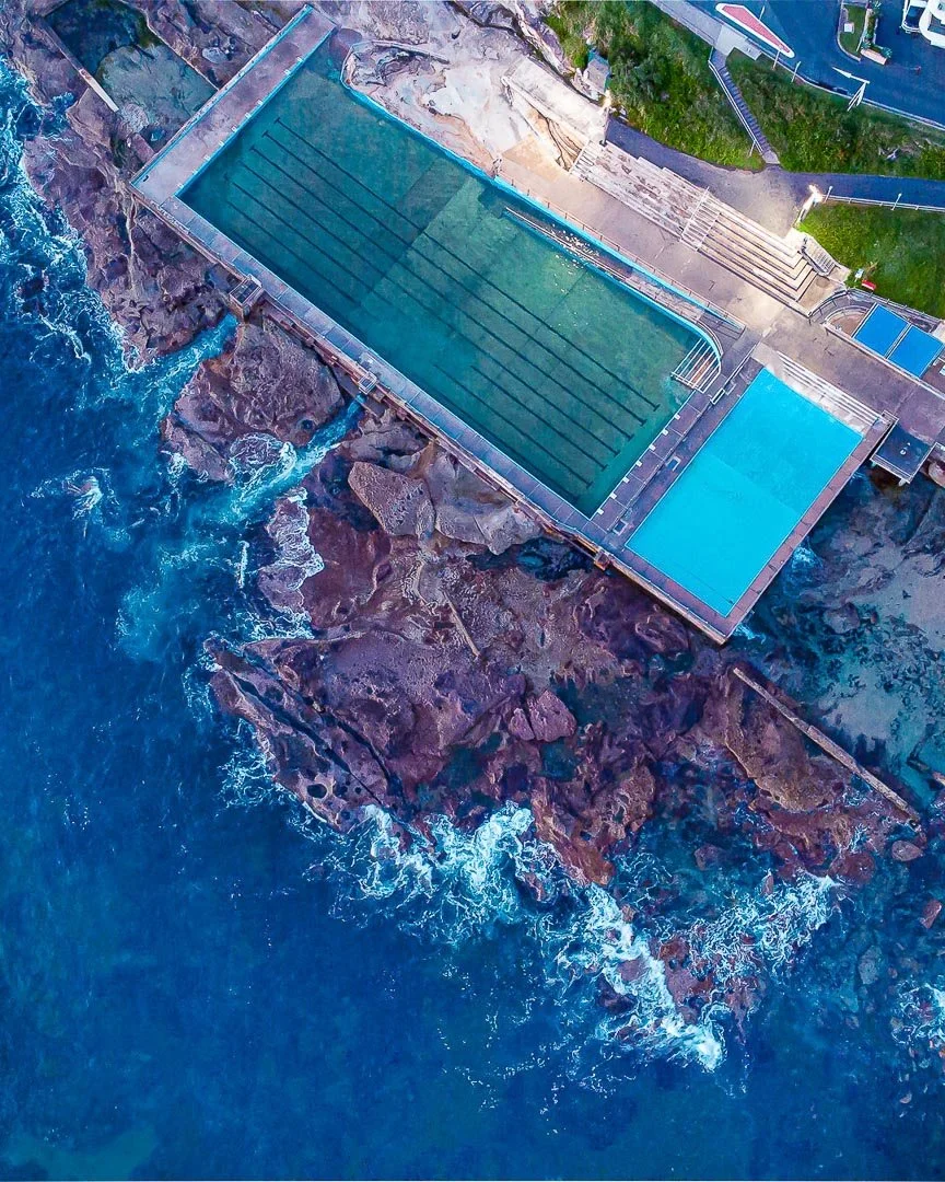 Dee Why swimming pool situated on a rocky shoreline, with a smaller pool next to it, surrounded by concrete decking and pathways.