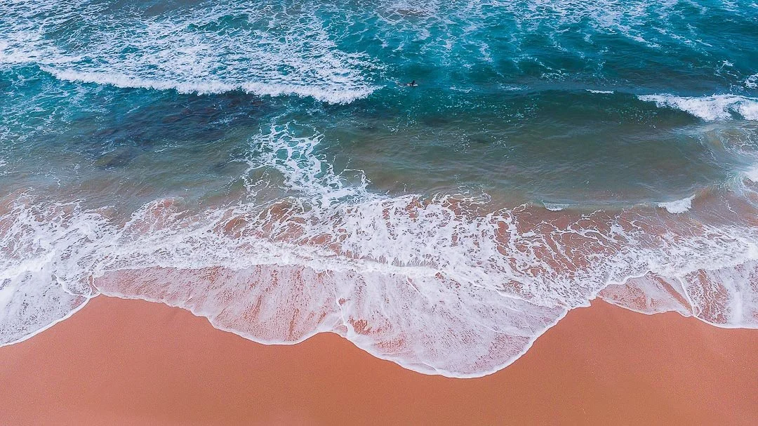 Aerial view of the ocean with waves hitting a sandy beach.