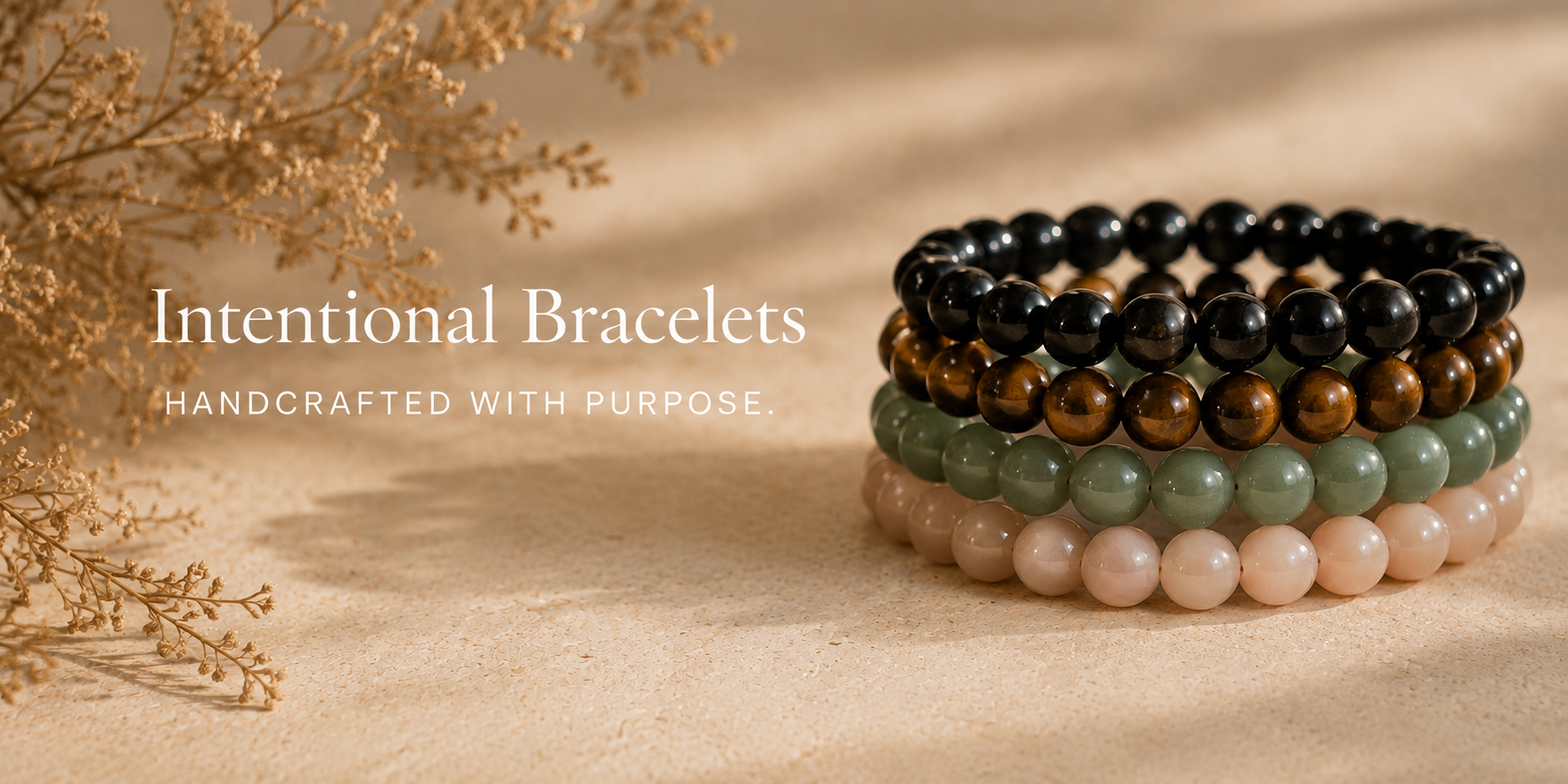 Stacked handcrafted beaded bracelets in black, brown, green, and pink, with dried beige flowers on the left, on a stone surface.