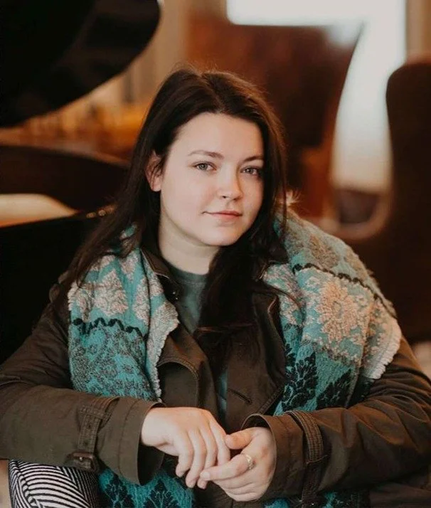 Ericka sits for a portrait with a soft smile and 10 o'clock stare. The lobby of a swanky hotel and piano are blurred behind her.