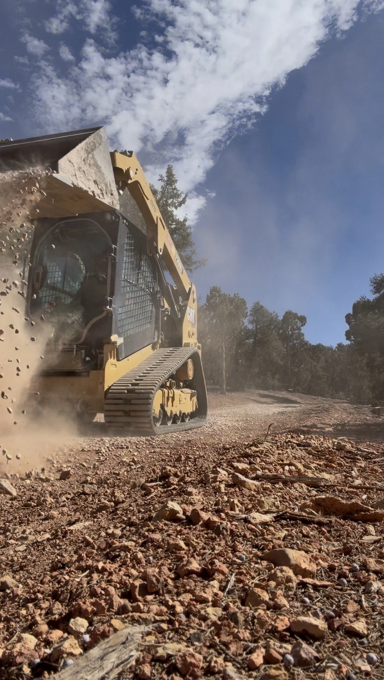 A yellow bulldozer moving dirt on a rocky landscape under a partly cloudy sky.