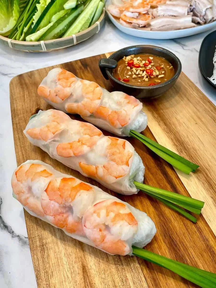 Fresh Vietnamese shrimp spring rolls with rice paper, shrimp, and herbs, served with a peanut dip and fresh vegetables.