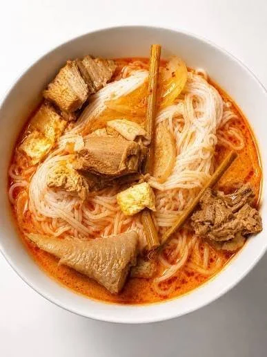 Bowl of noodle soup with broth, rice noodles, chunks of meat, and pieces of tofu or vegetables.
