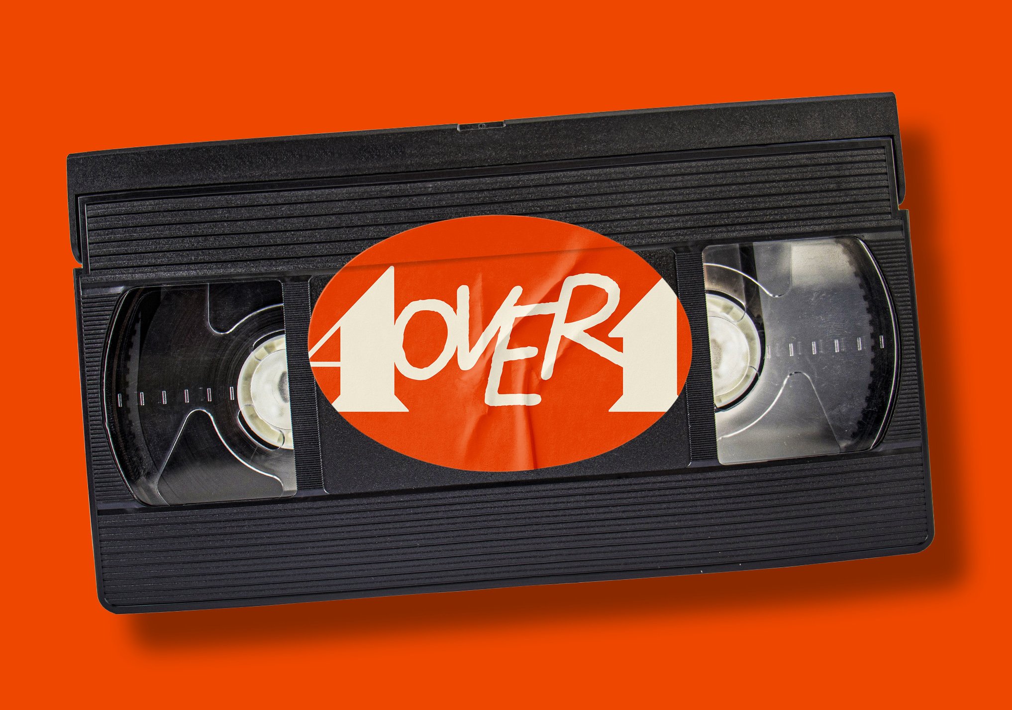 Close-up of a VHS tape with a bright orange sticker and bold white handwritten text that says '4over1' on a solid bright orange background.