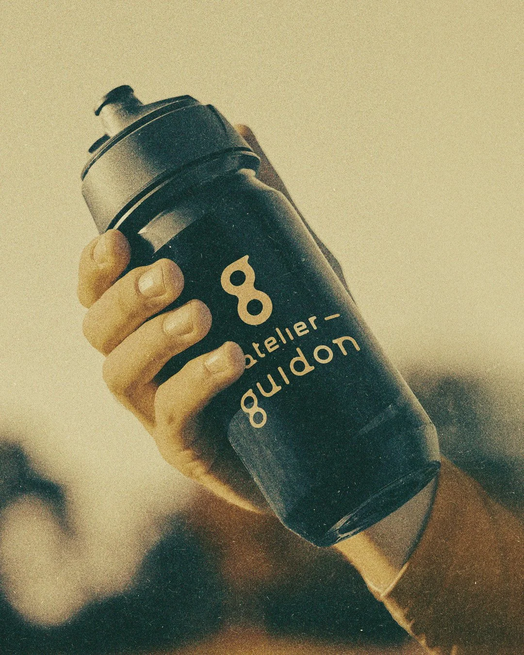 Person holding a biker's bottle, featuring a logo with the words ' Atelier Guidon'.