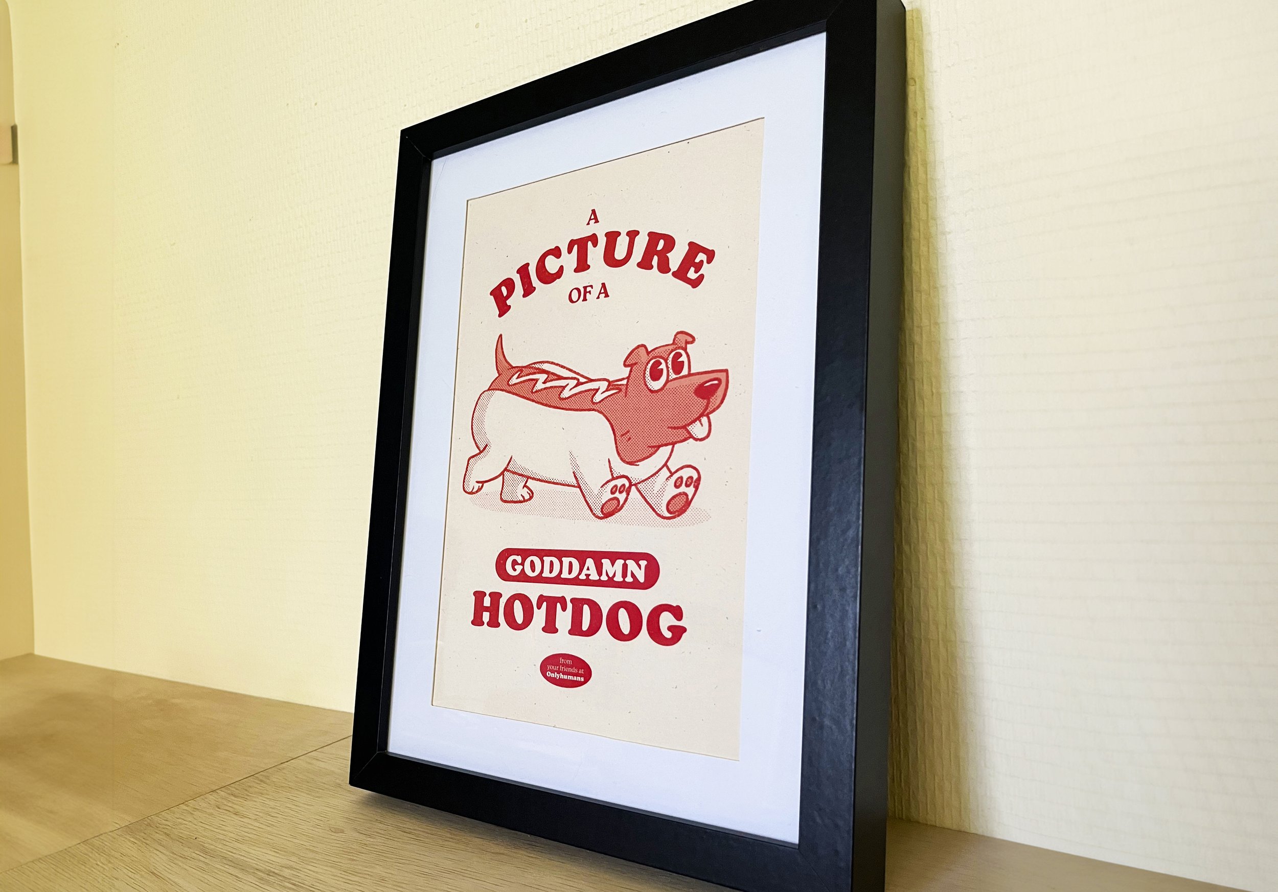 Framed sign with red text and cartoon dog/hot dog hybride. The sign reads: 'A PICTURE OF A GODDAMN HOTDOG'.