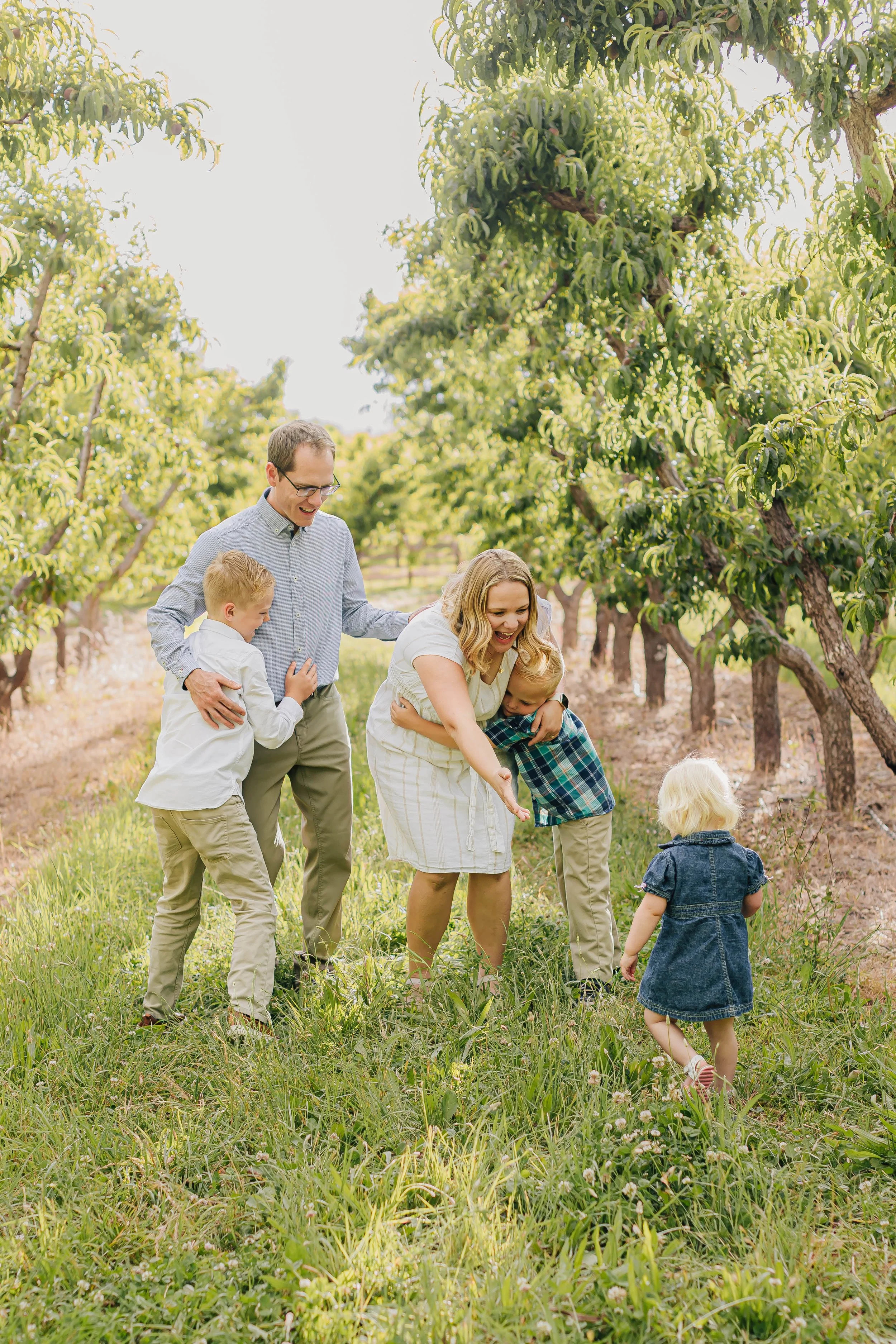 Family of five playing in a lush green field near fruit trees on a sunny day