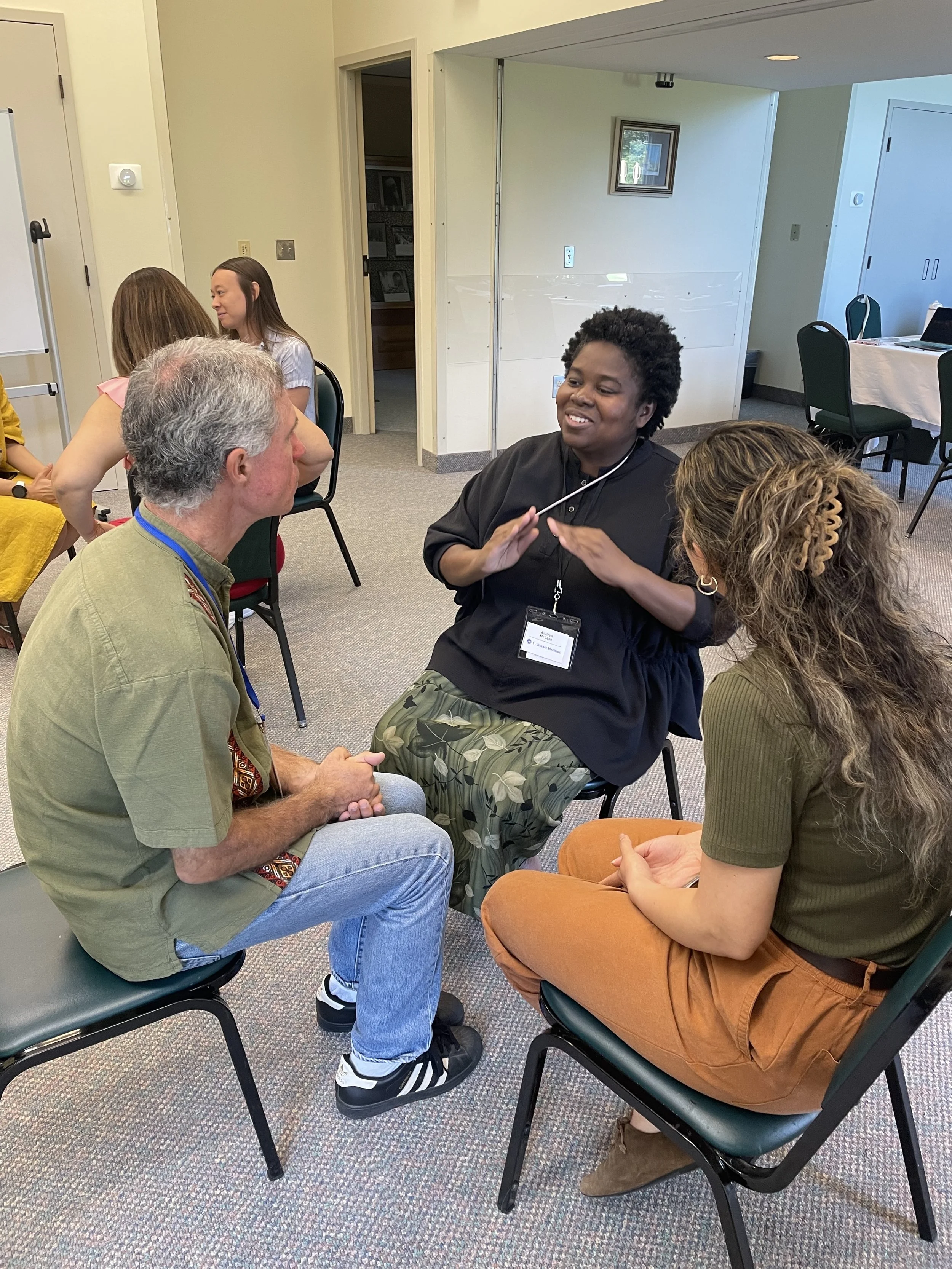 A group of diverse people sitting in a circle, engaged in a conversation in a meeting room.