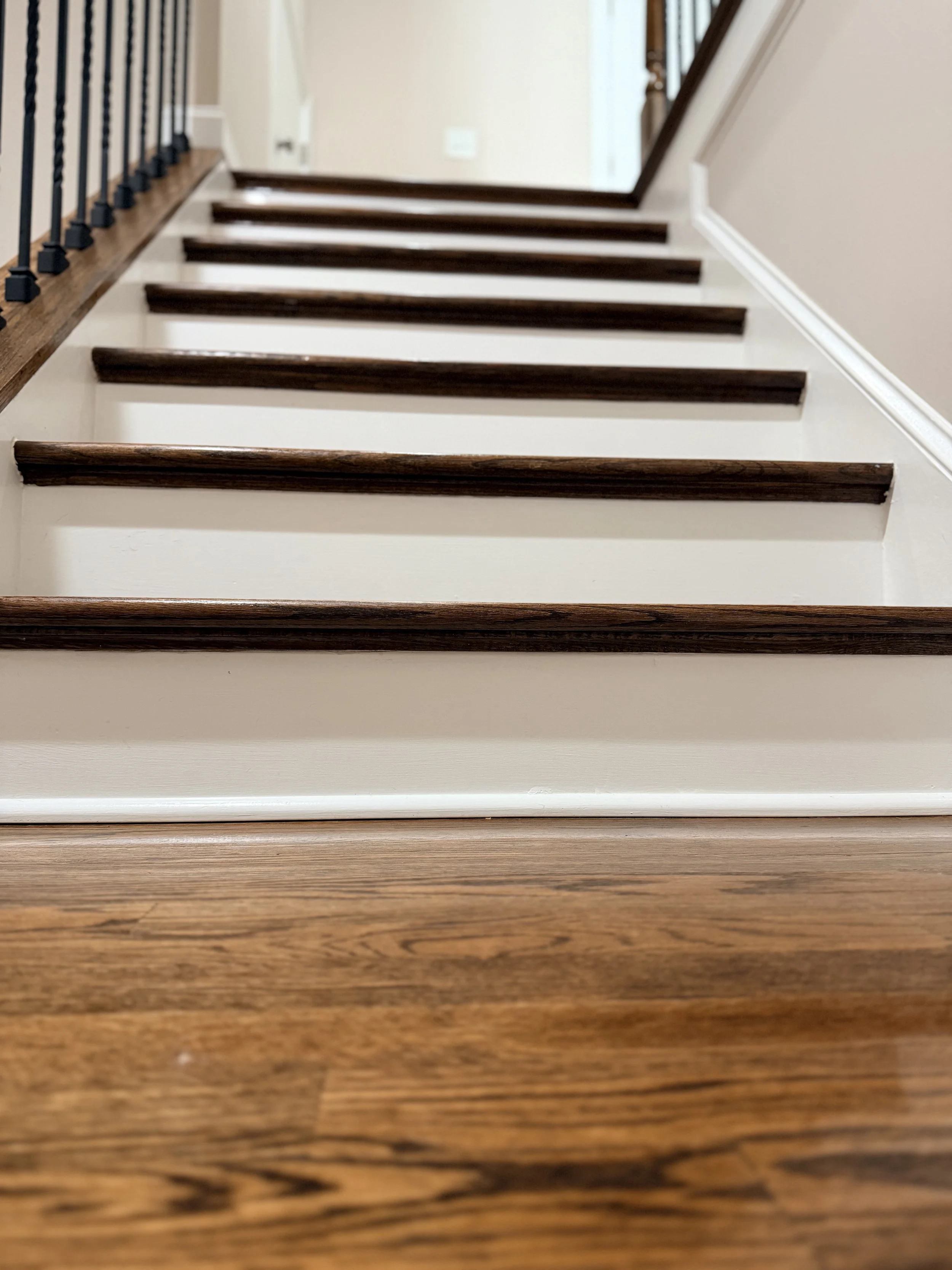 Interior staircase with wooden steps and dark brown handrails, viewed from below at the bottom of the stairs.