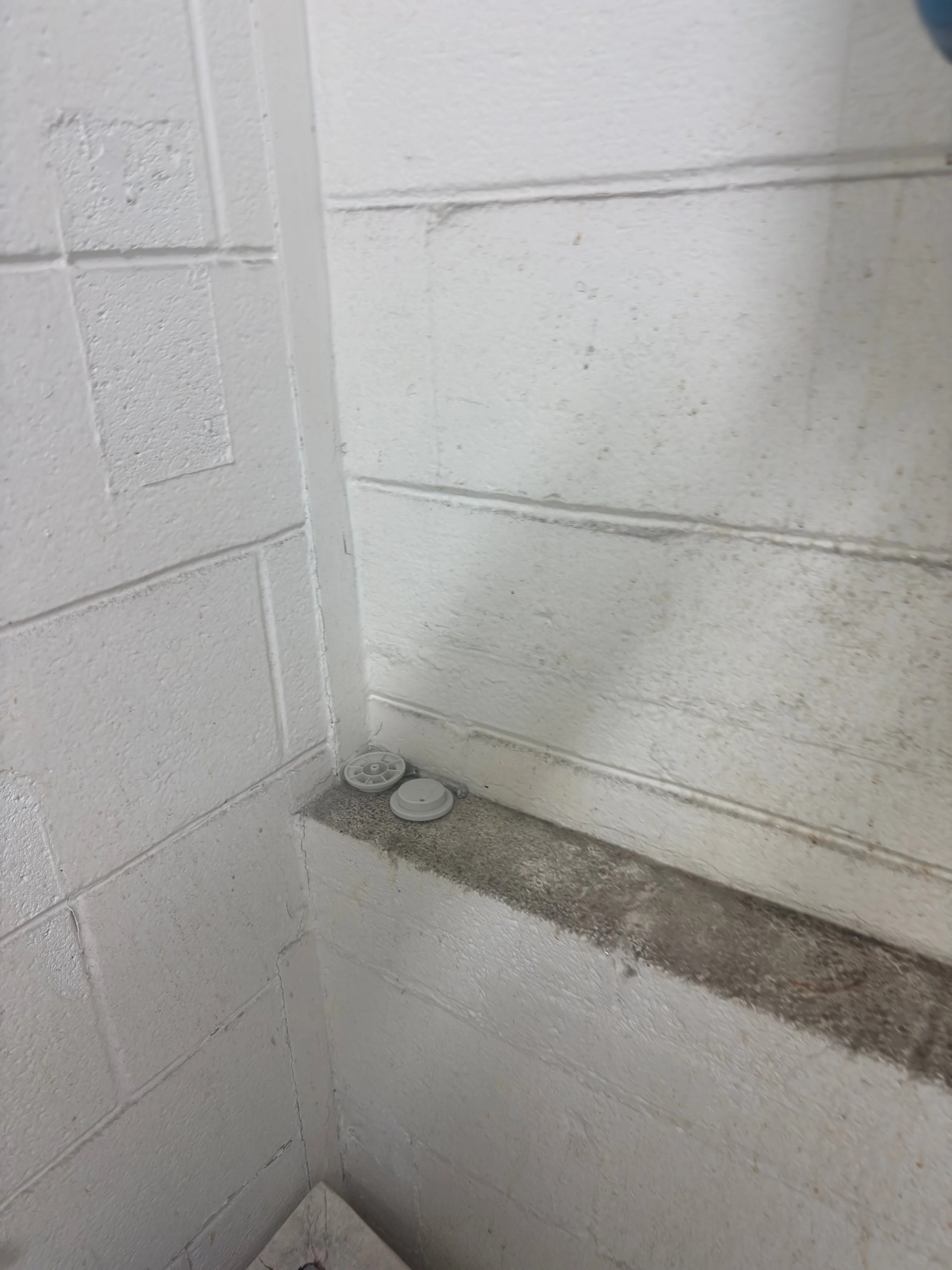 Before view of dark dust, grease, and industrial grime buildup on a concrete masonry block restroom wall ledge at a ULCS facility.⁠