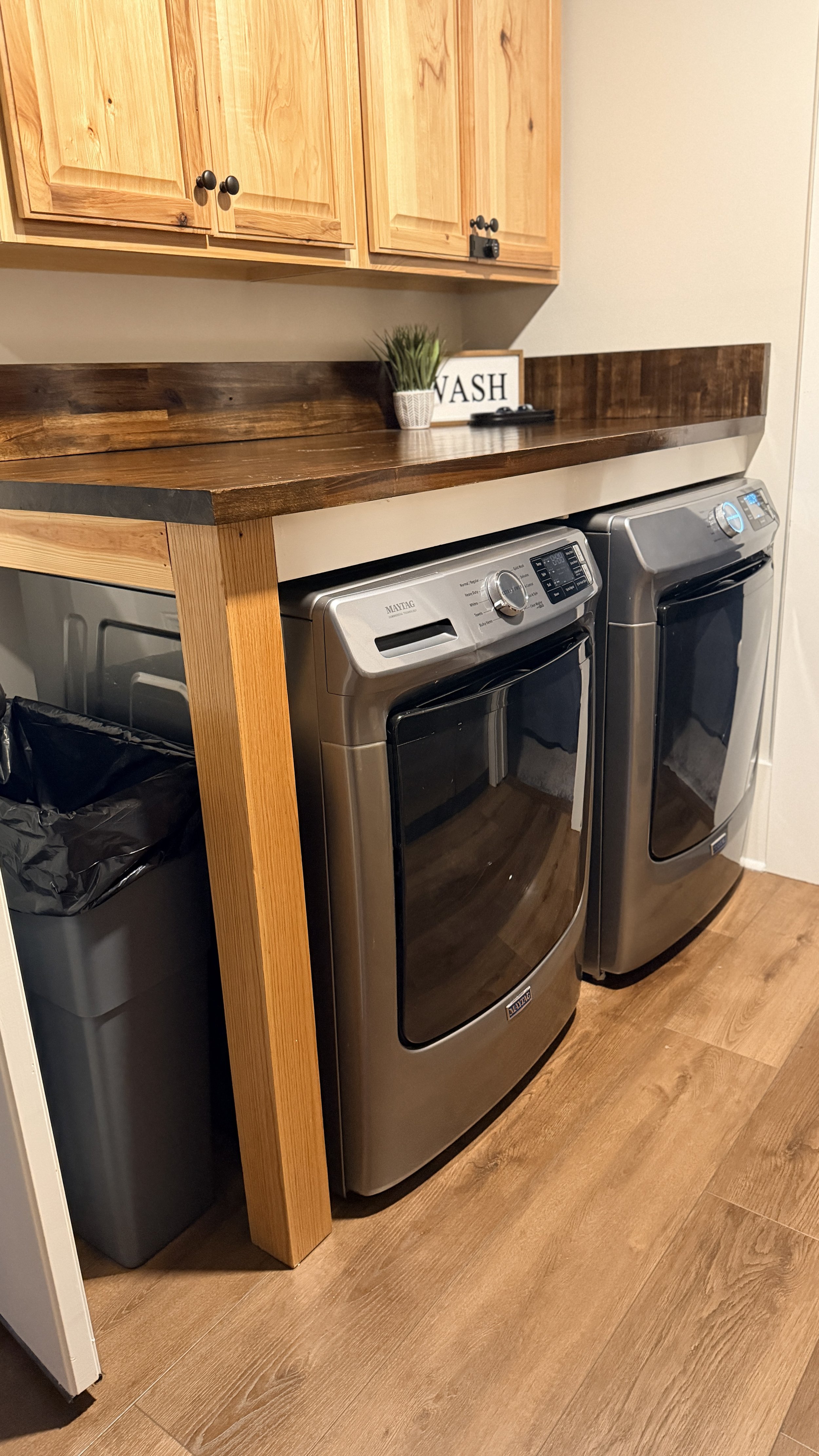 An immaculately cleaned and wiped-down laundry workstation with a spotless wooden counter and sanitized stainless steel washer and dryer units.⁠