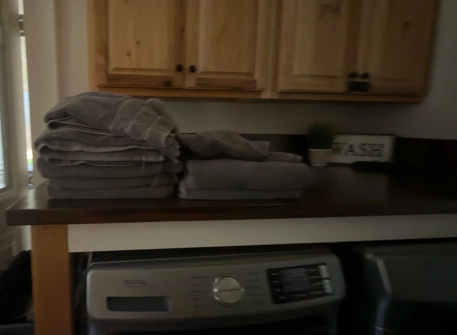 Used guest towels piled on a wooden laundry folding counter on top of a washing machine before an Airbnb turnover service.⁠