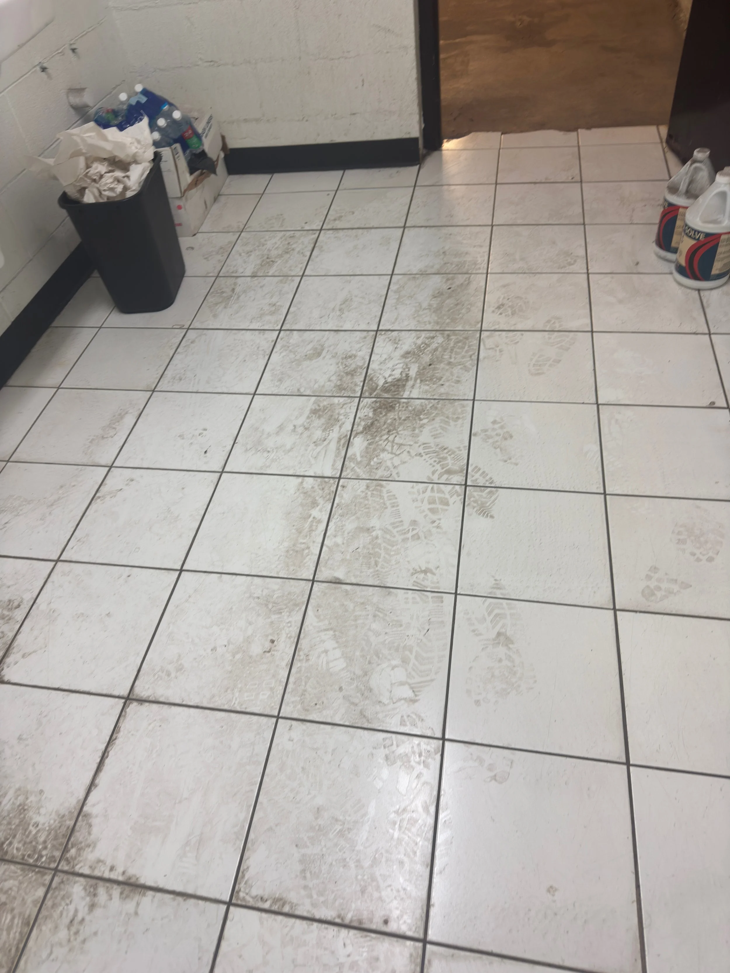 Before view of heavy mud tracking, grease stains, and embedded industrial debris across a high-traffic restroom tile floor at ULCS.⁠