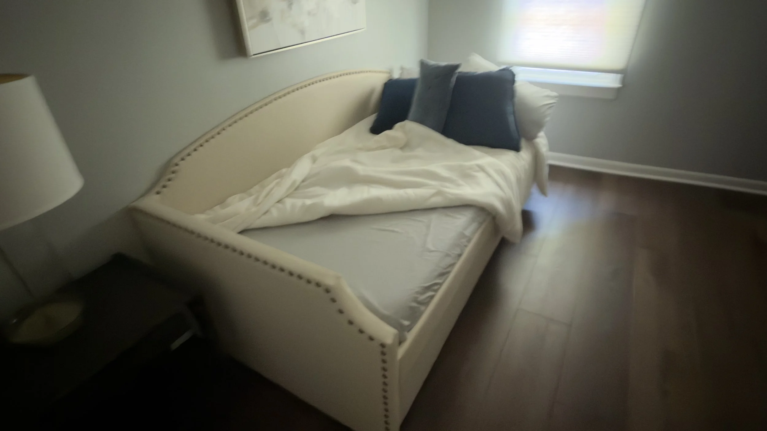 An unmade upholstered cream daybed with rumpled sheets and unkempt blankets inside an Airbnb bedroom prior to a professional turnover clean.⁠