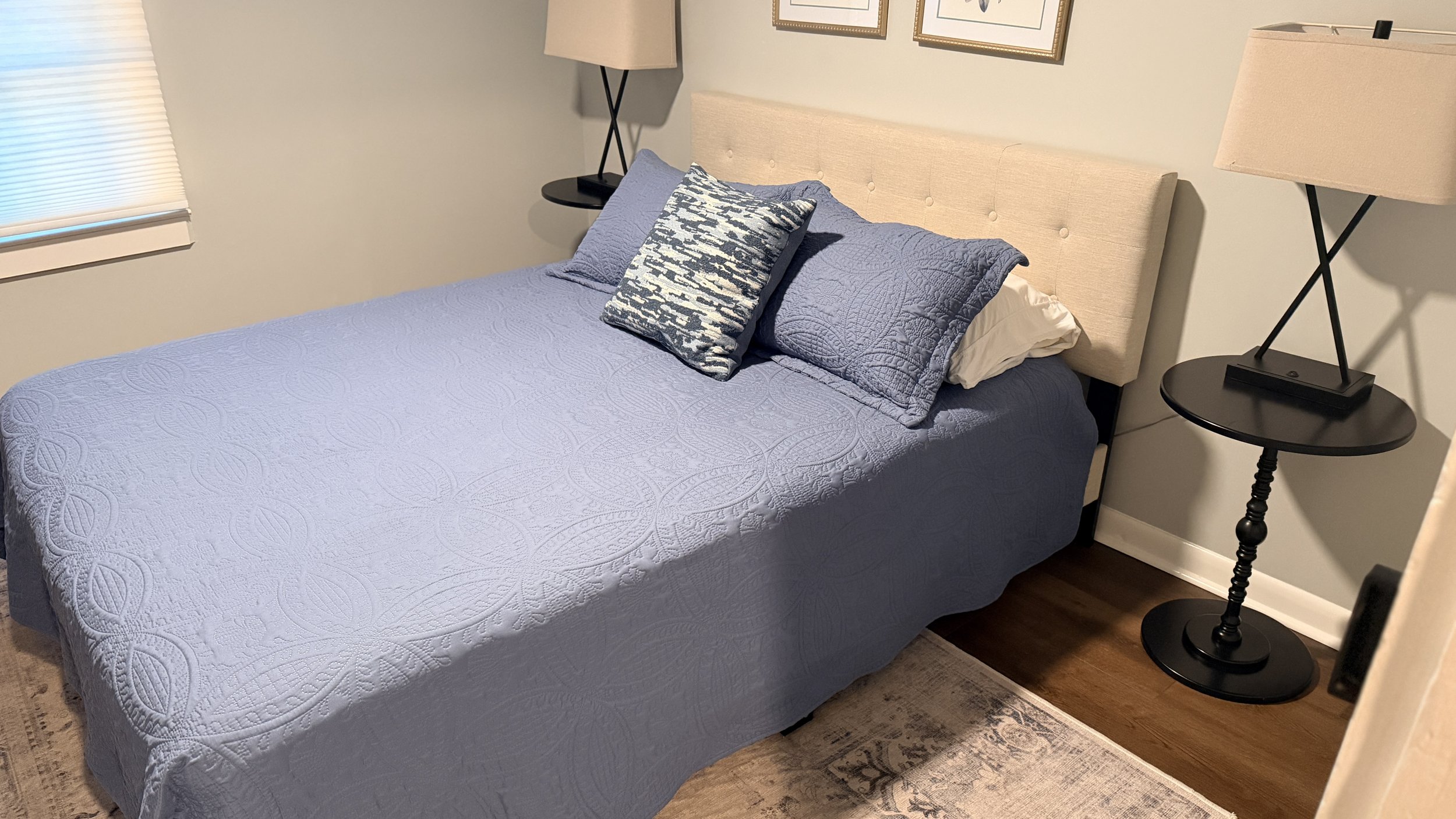 ⁠A perfectly made bed featuring freshly washed and dried white linens, a tufted beige headboard, and neatly styled blue patterned pillows.⁠