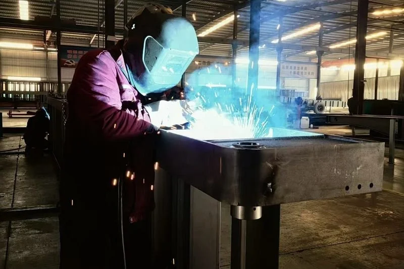Worker welding metal at an industrial workshop while wearing safety gear.