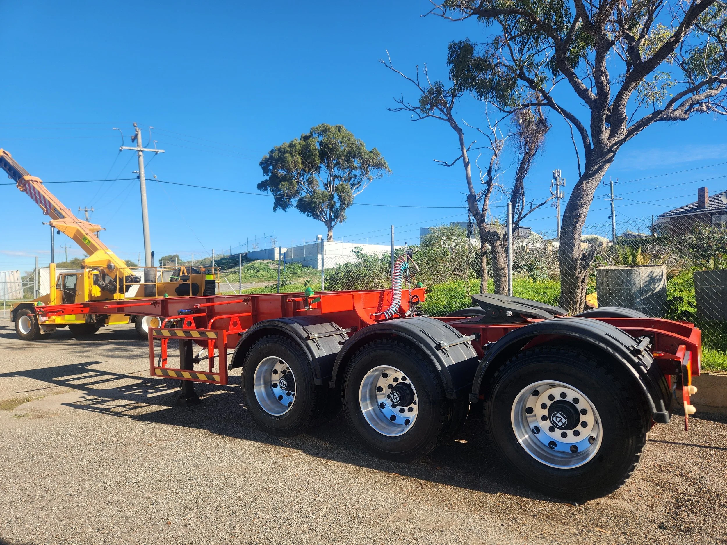 A flatbed truck with large black wheels parked outside, with trees, utility poles, and a clear blue sky in the background.