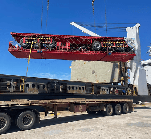 A large piece of machinery being lifted onto a flatbed truck by a crane