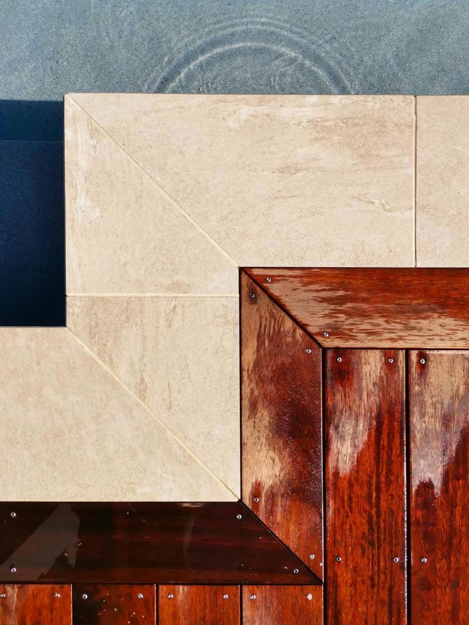 A close-up shot of a wall with three distinct sections of different materials: a dark gray section at the top, a beige stone section in the middle, and a rich, polished dark wood section at the bottom, with visible screws securing the wood panels.