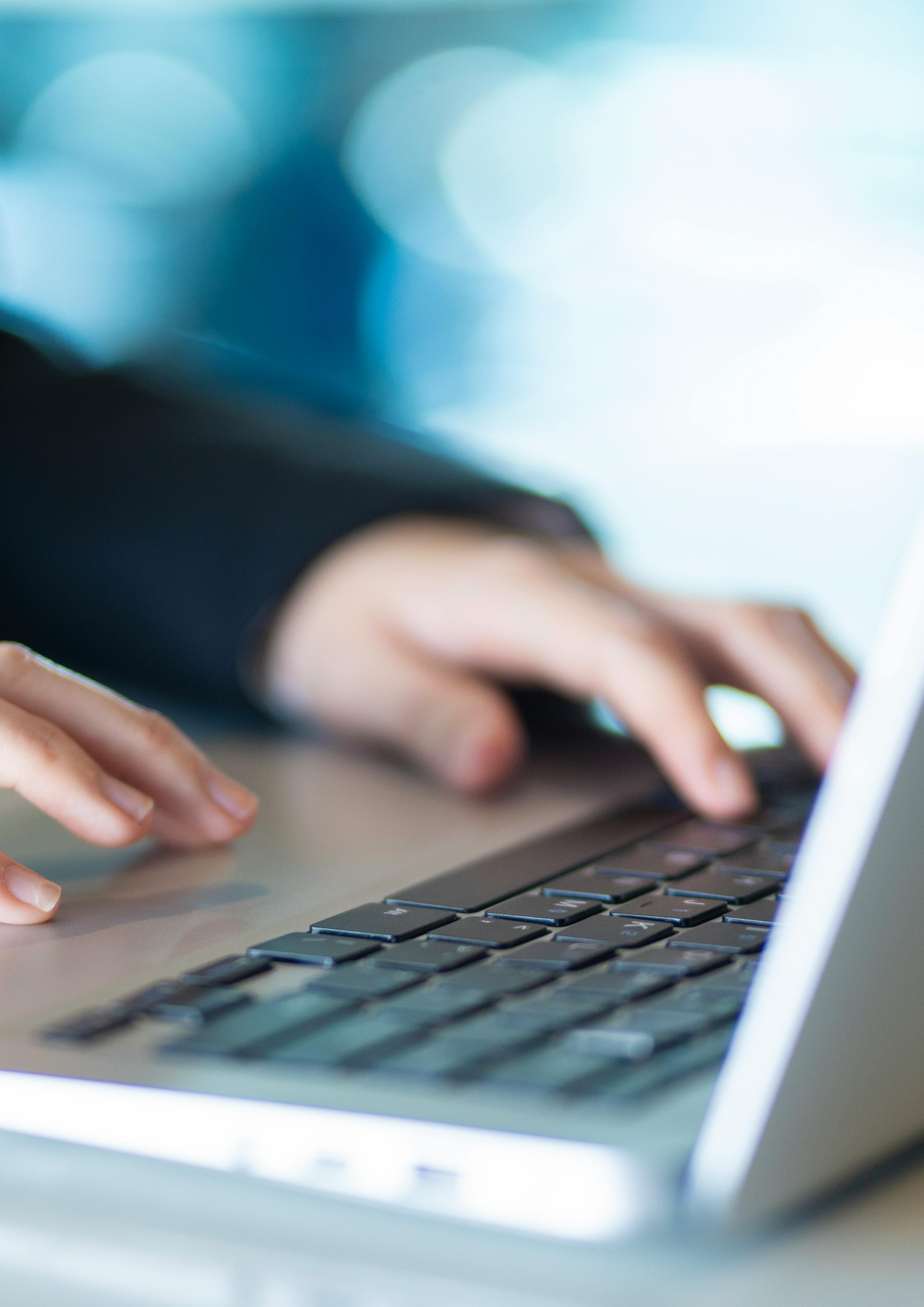 Close-up of a person's hands typing on a laptop keyboard.