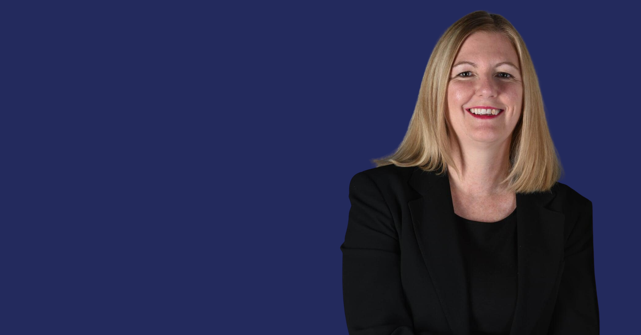 A woman with blonde hair wearing a black blazer smiling against a plain dark blue background.