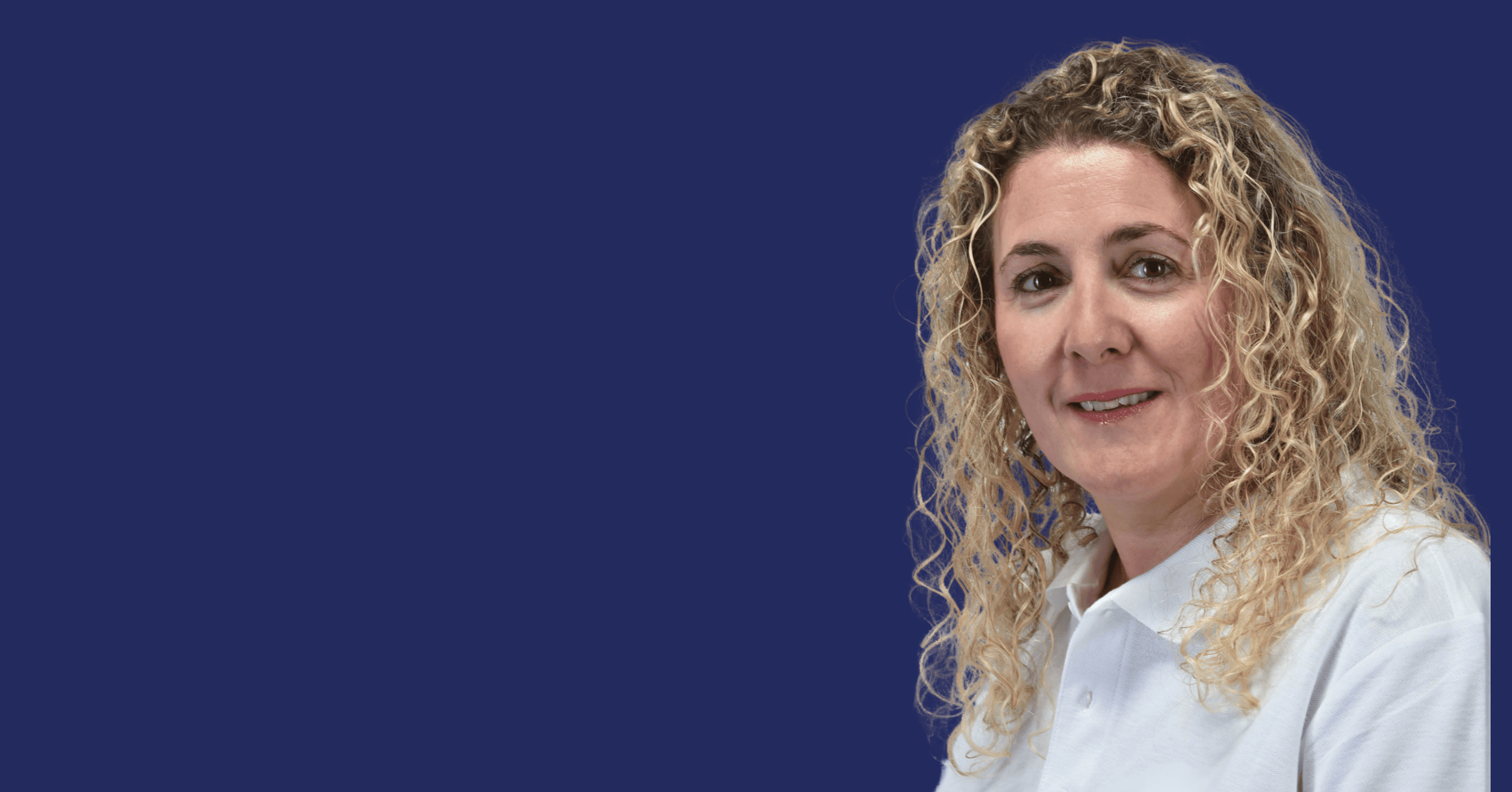 A portrait of a woman with curly blonde hair, smiling, wearing a white shirt, against a blue background.