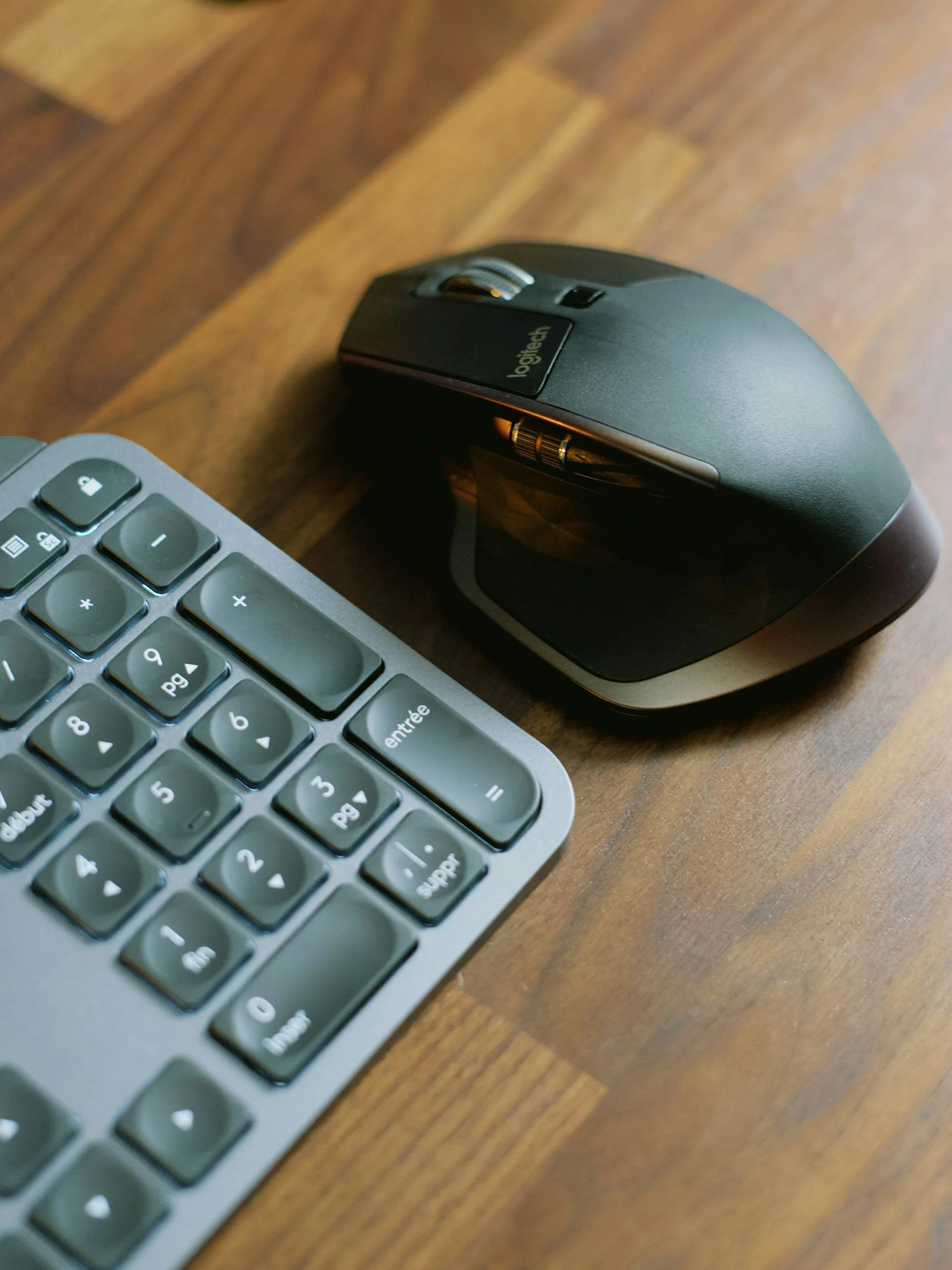 Close-up of a computer mouse and a keyboard on a wooden desk.