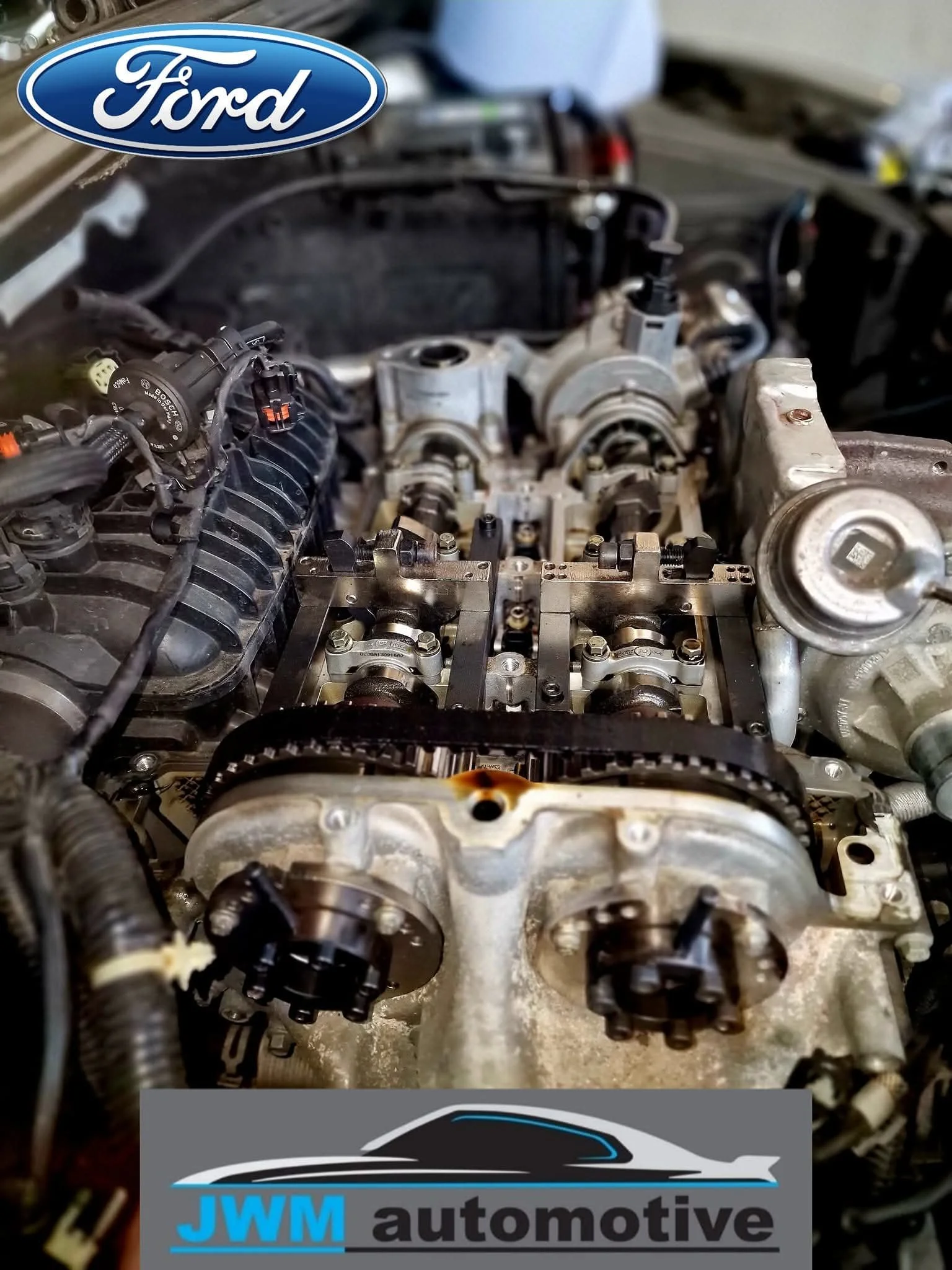 Close-up of an engine with components and timing chain visible, with a Ford logo and a banner that reads "JWM automotive" at the top.
