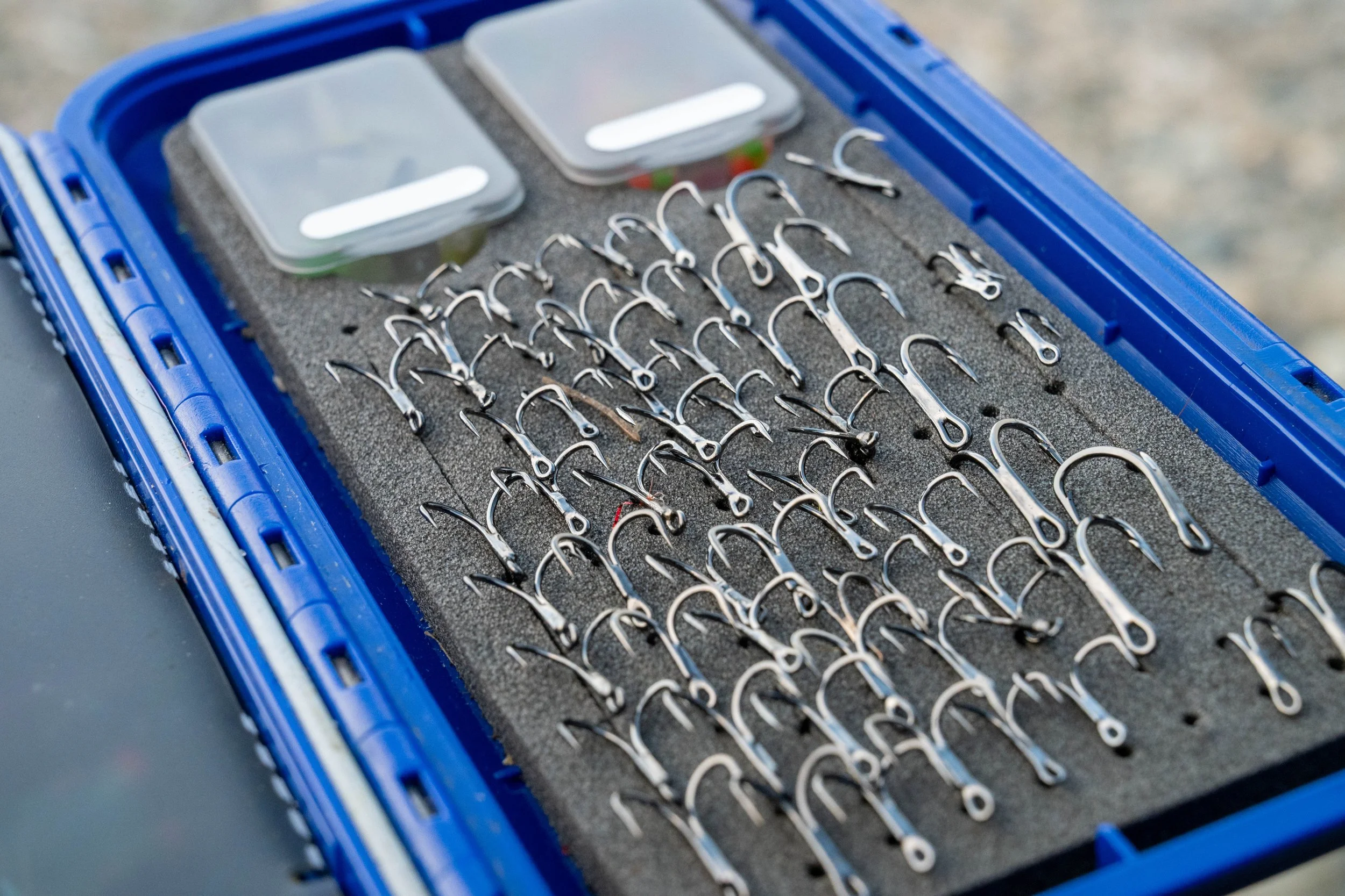 A blue tackle box containing fishing hooks and two small plastic containers with lids.