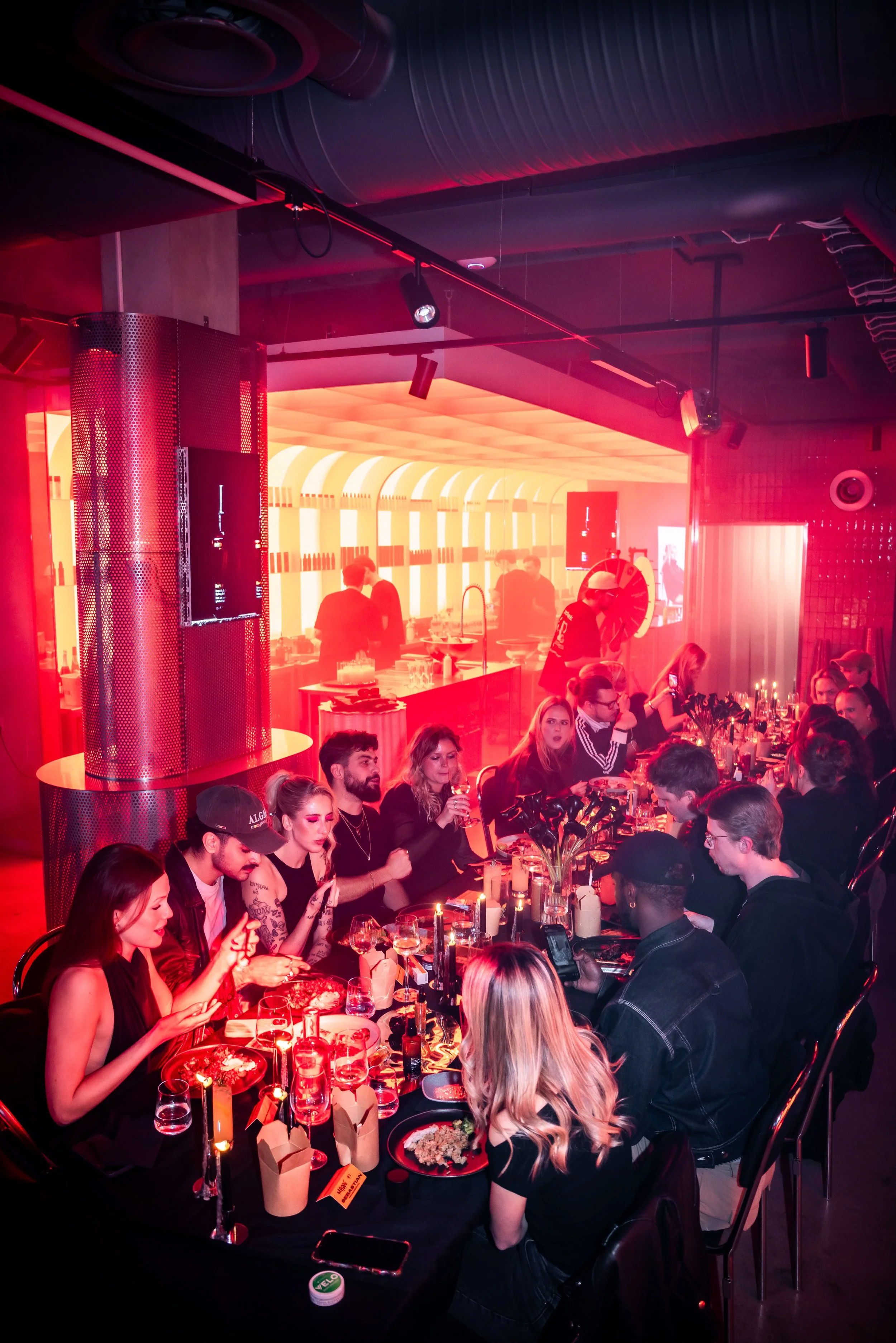 En livlig restaurang eller bar med många gäster som äter och dricker, med röd belysning och modern inredning.