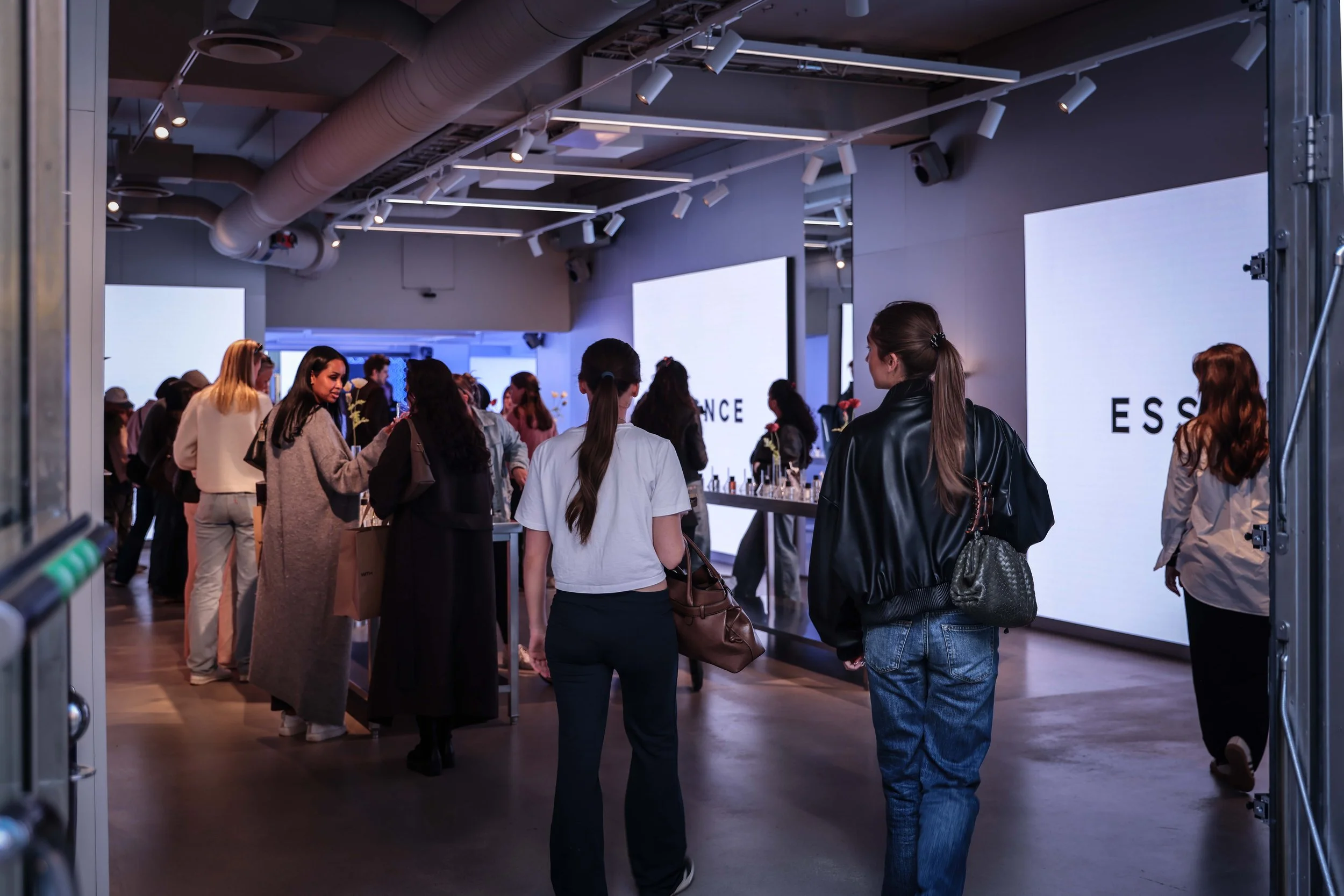 Folk samlade i ett rum med stora vita skärmar, som visar texten 'ESS' och 'NCE', troligen på en mässa eller ett event.