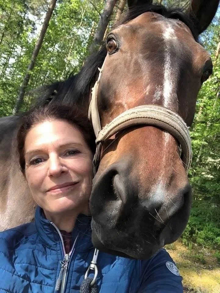 Kvinna och häst nära varandra i en skog.