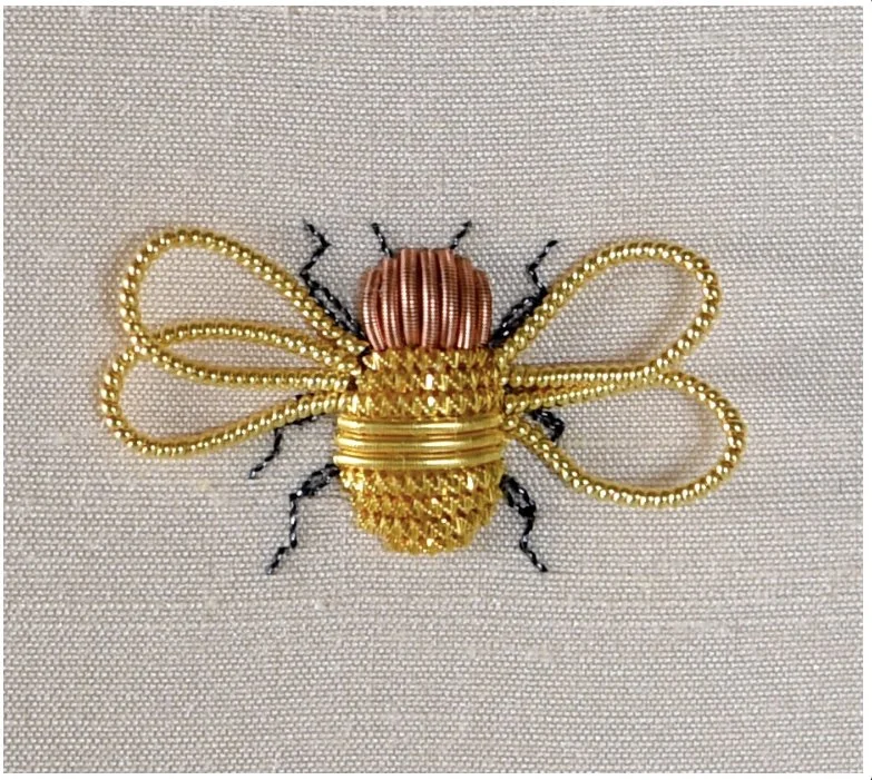 Embroidered bee with golden wings, a copper head, and black legs on fabric