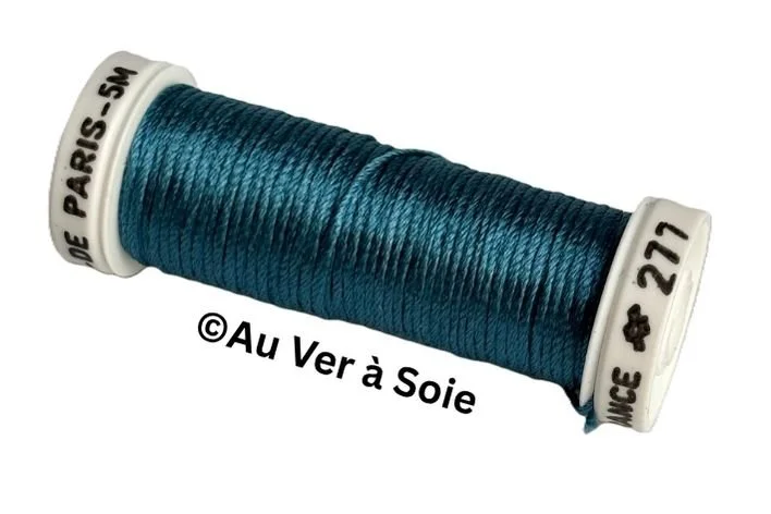 A spool of dark teal silk thread, labeled with French text and numbers, with a copyright notice from Au Ver à Soie.