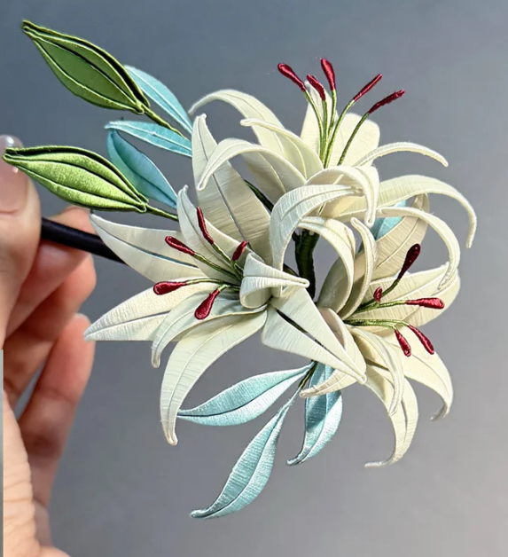 Fabric lily flower bouquet with white, blue, and green leaves and red-tipped stamens.