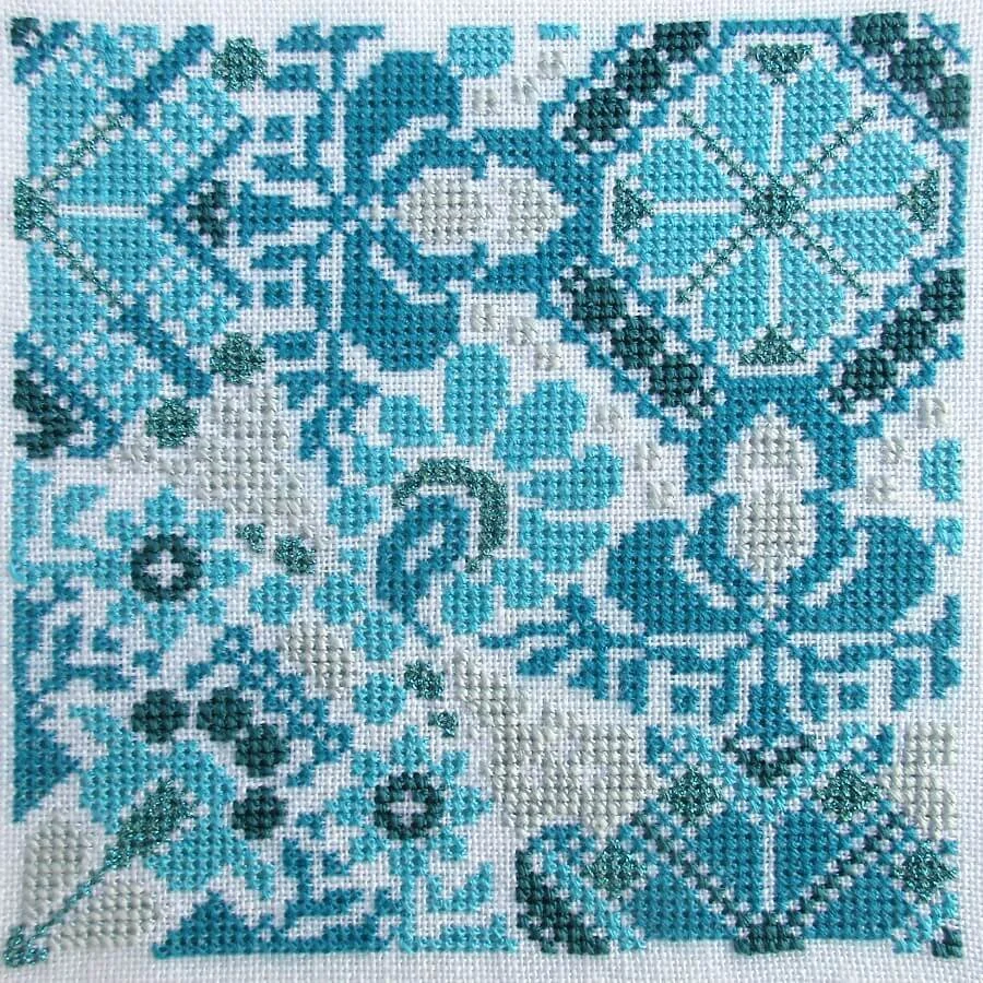 A detailed cross-stitch embroidery pattern featuring various geometric and floral designs in shades of blue and white.