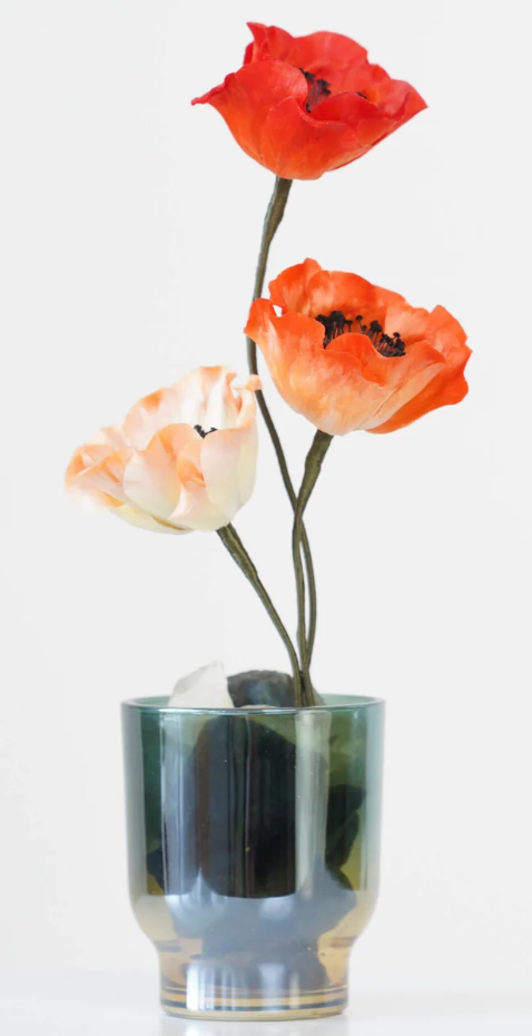 A glass vase with three artificial poppy flowers in shades of red, orange, and cream