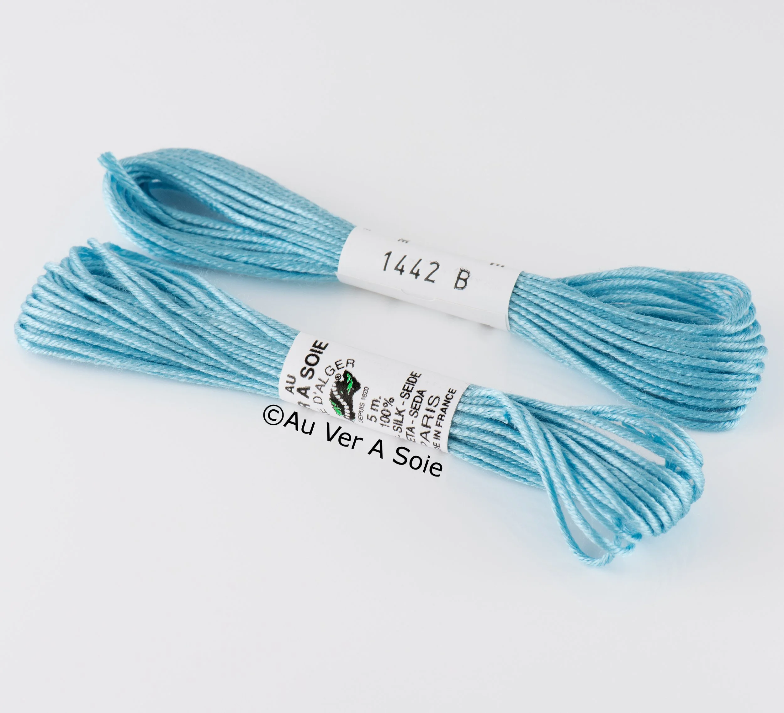 Light blue embroidery floss or thread lying on a white surface with a white label featuring black text wrapped around the skein.