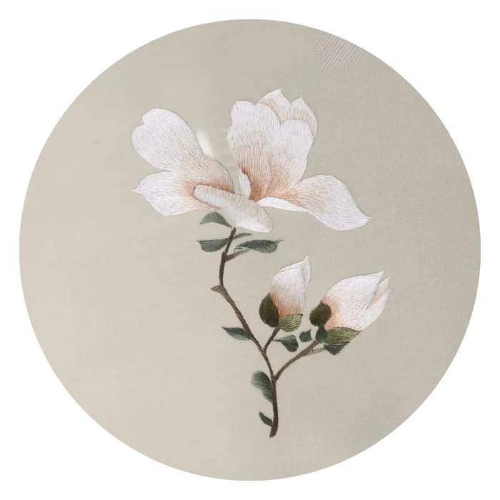 Embroidery of a cotton plant with white flowers and green leaves on a beige circular background.
